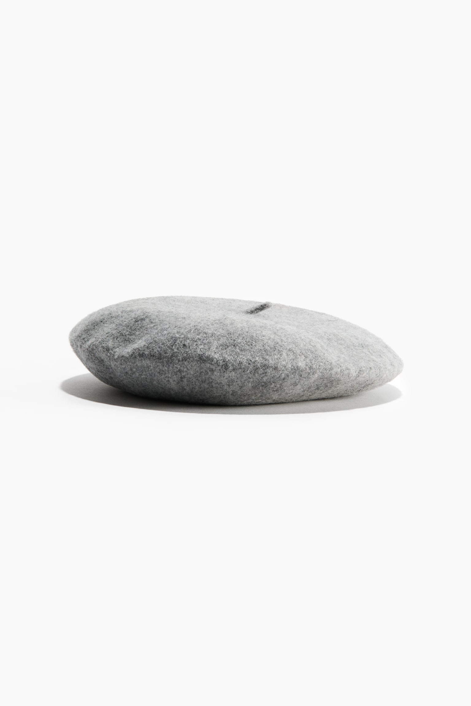 A grey felted wool beret is resting flat, showcasing its classic rounded shape and soft textured finish. The beret features a small matching wool stalk at the centre top.