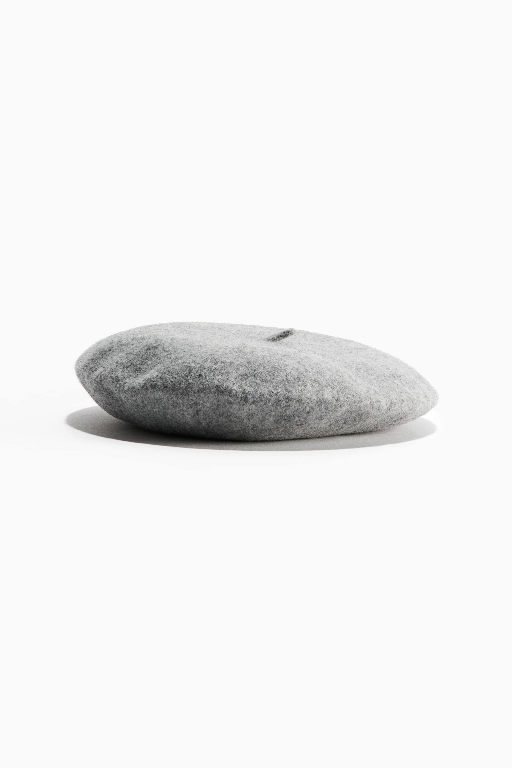 View larger image: A grey felted wool beret is resting flat, showcasing its classic rounded shape and soft textured finish. The beret features a small matching wool stalk at the centre top.