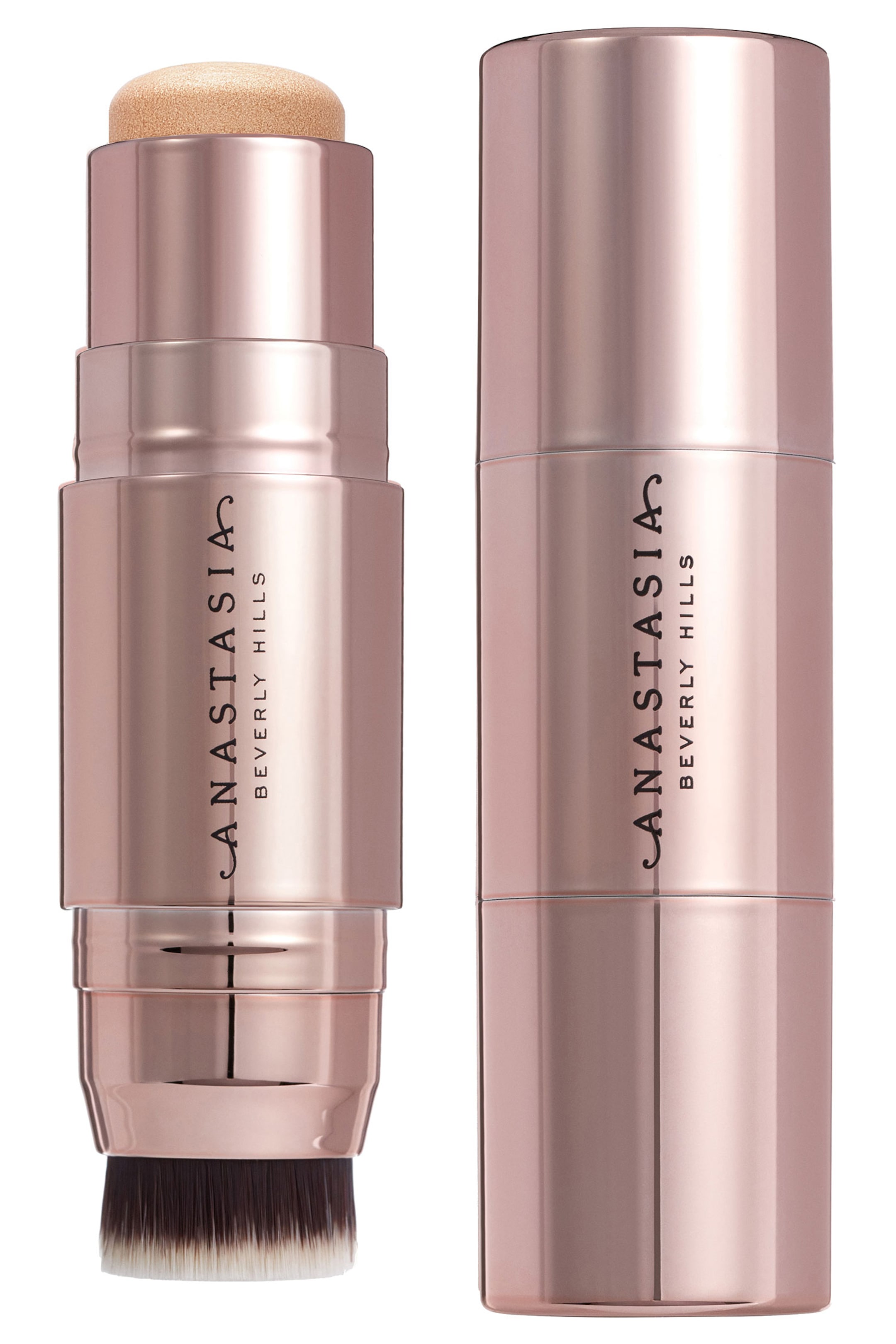 Vis større bilde: To Anastasia Beverly Hills sminkestifter står oppreist, begge med sylinderformet emballasje i roségull-toner med merkevarenavnet trykt vertikalt. Stiften til venstre er åpen og avslører en lys beige, rund svampapplikator på toppen og en børste med mørke til hvite børstehår som strekker seg fra bunnen, mens stiften til høyre forblir lukket.