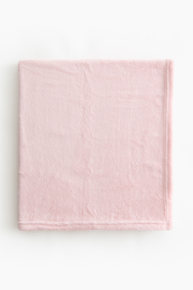 A light pink baby blanket is folded into a rectangle. Its soft fleece texture is visible across the surface, and its edges are neatly finished. - 1