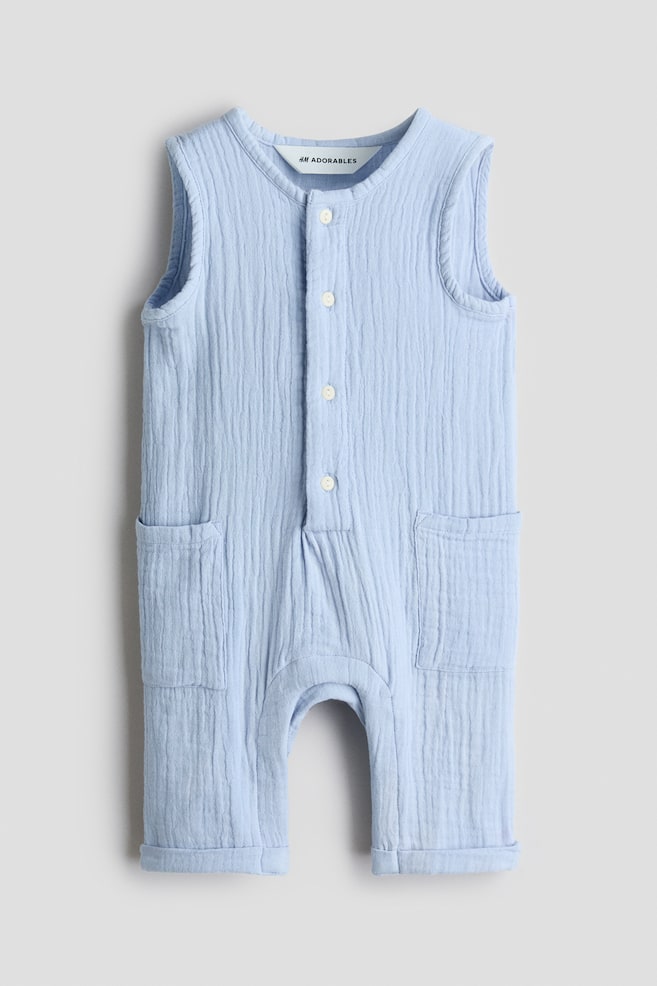 An H&M Adorables light blue crinkled muslin sleeveless romper suit is facing front, featuring a round neckline, buttons down the front, and two open patch pockets on the sides. The leg hems are showing sewn-in turn-ups. - 1
