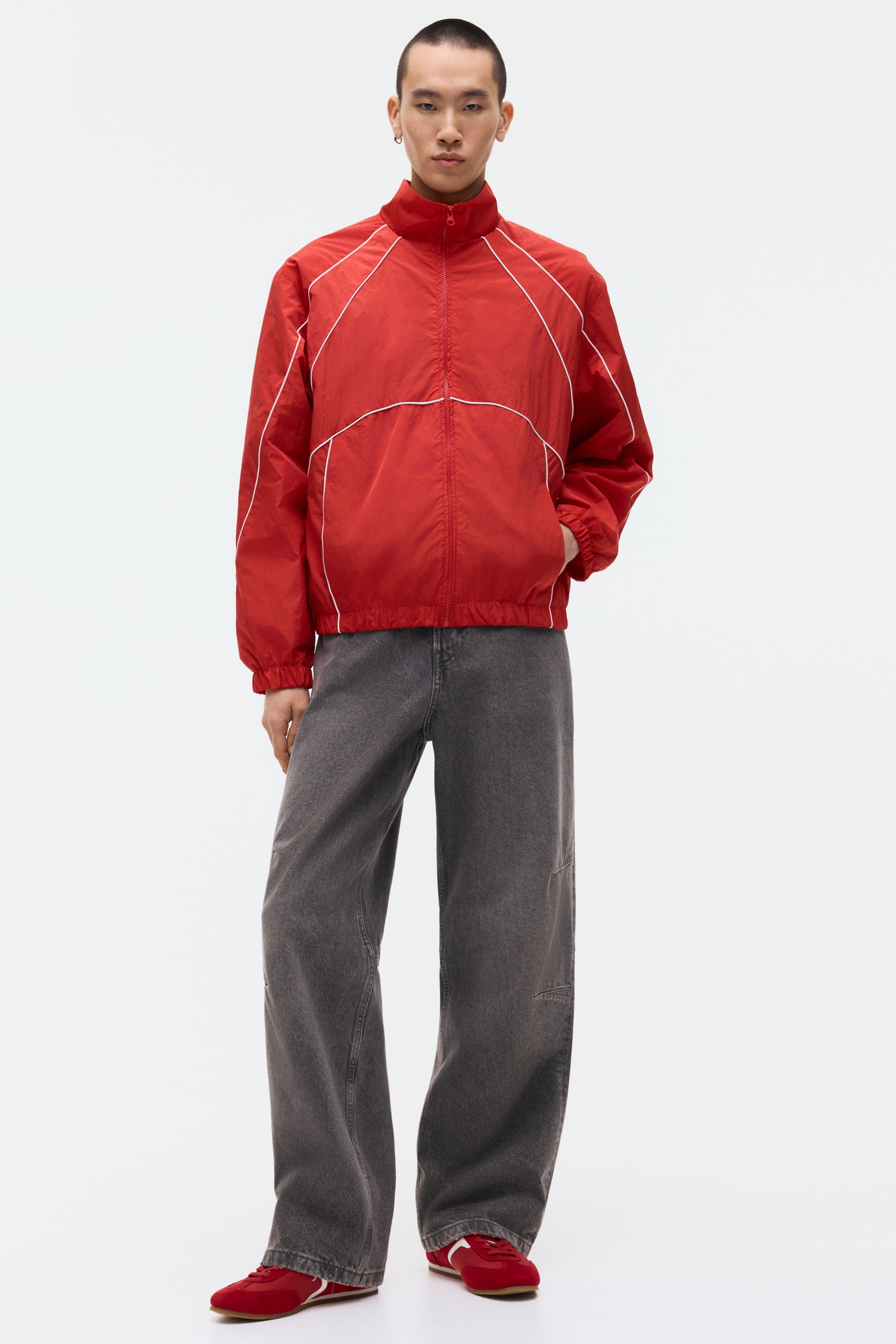 Agrandir l'image: La veste de survêtement rouge est dotée d'un col montant et d'une fermeture éclair intégrale sur le devant. Des passepoils blancs courent le long de la poitrine, des épaules et des manches, tandis qu'un ourlet et des poignets élastiqués sont également visibles, avec des poches latérales.