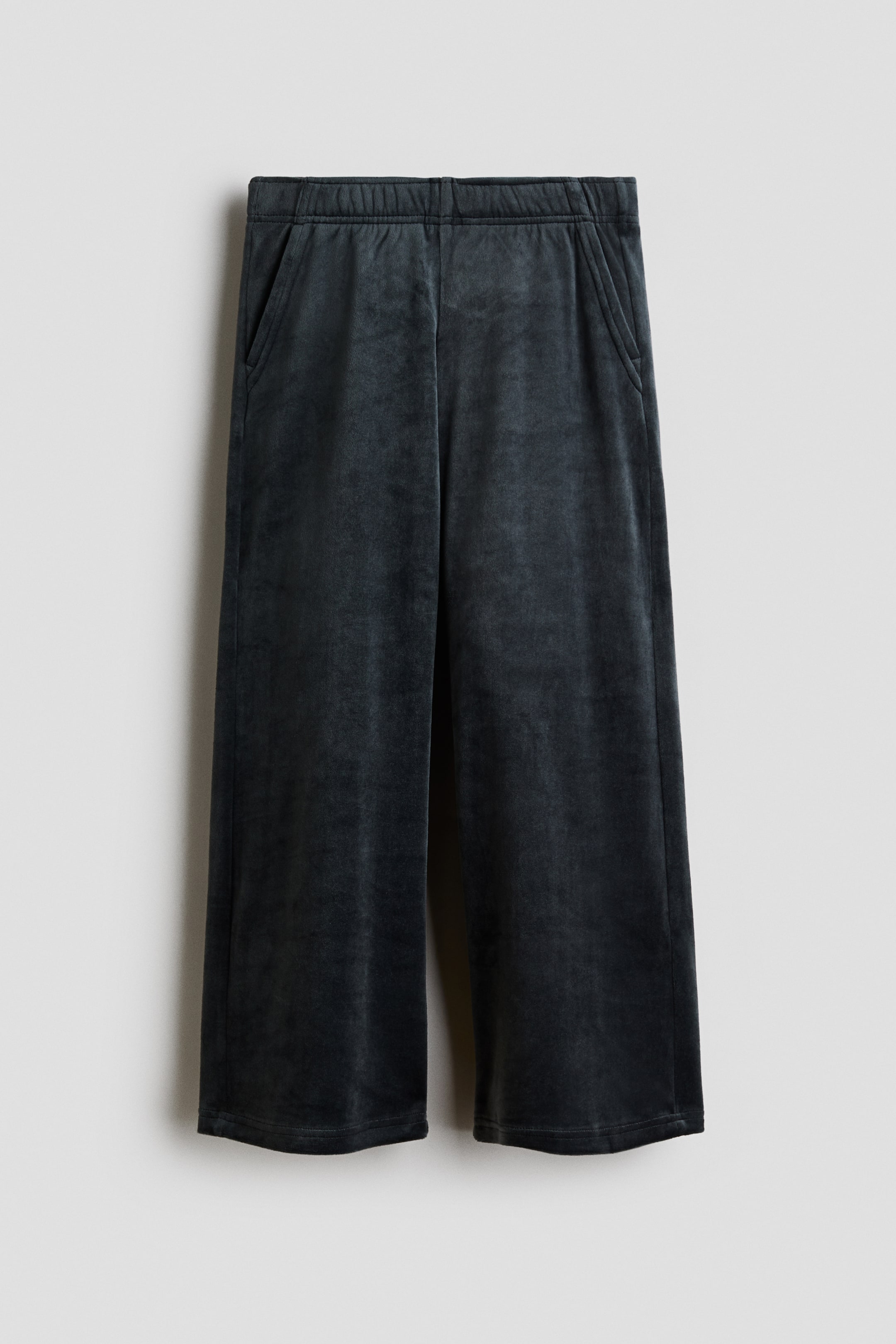 View larger image: A front view of dark gray velour joggers featuring an elastic waistband, diagonal side pockets, and straight legs. The pants are displayed flat to highlight their soft texture and relaxed structure.