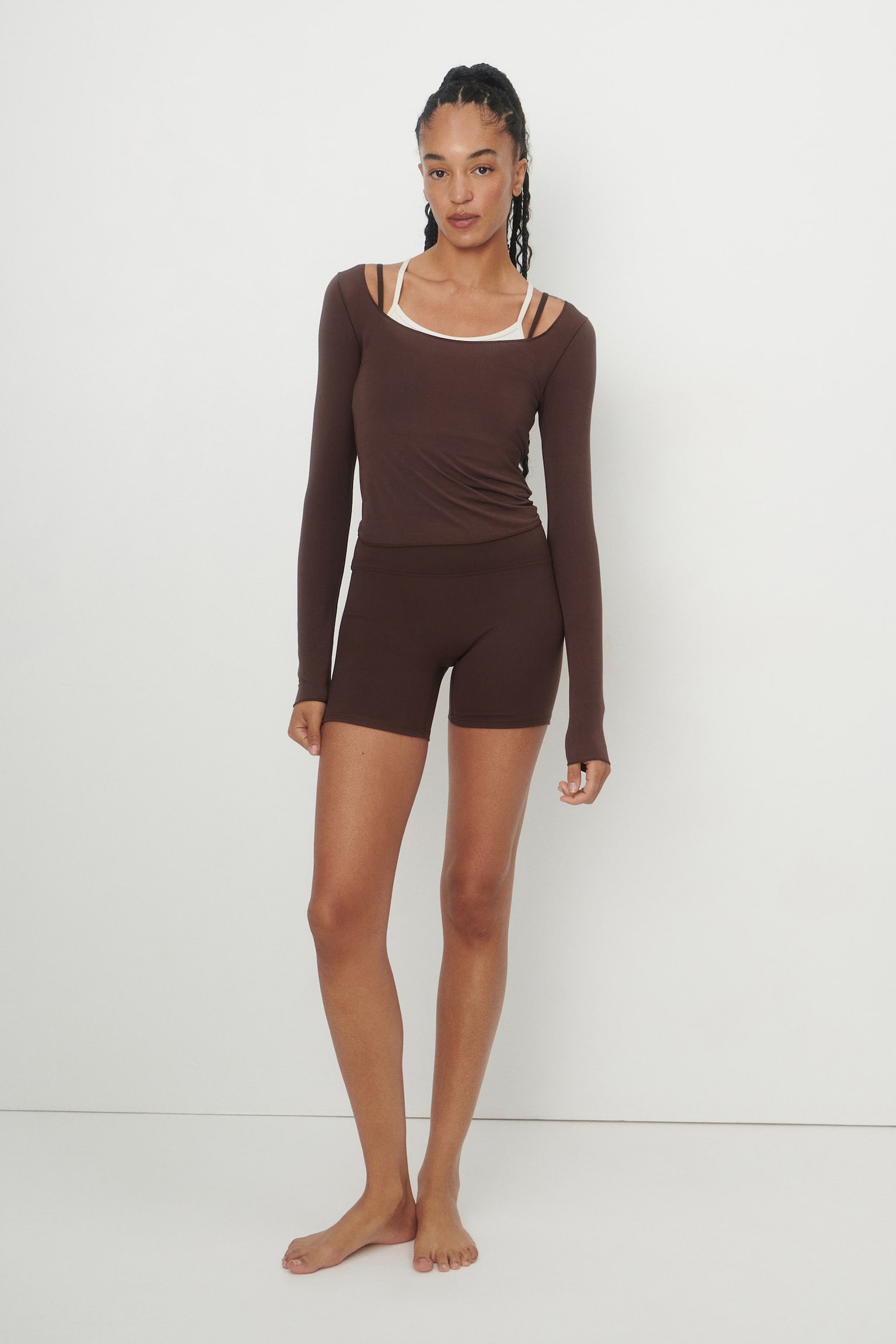 A brown long-sleeve top is laid flat and facing front, featuring a scoop neckline. It presents a cropped length with a raw-edge hem. - 1