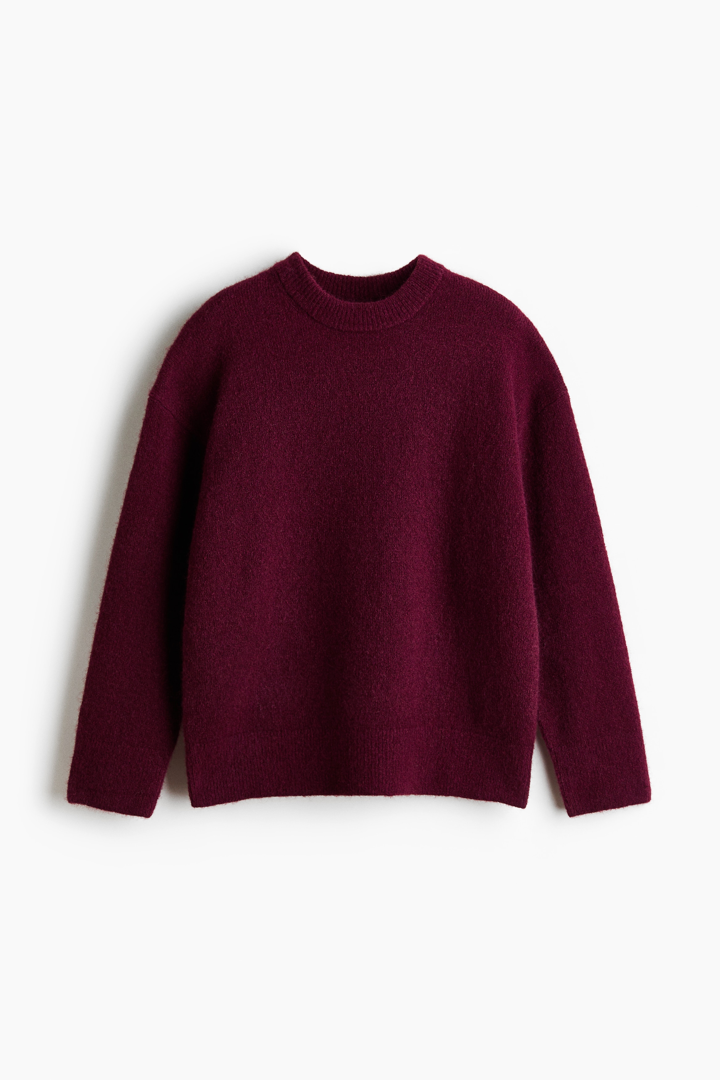 La modelo lleva un jersey holgado en color burdeos, confeccionado en un punto suave y afelpado, y posa con ambos brazos levantados. El jersey presenta cuello redondo, hombros caÃ­dos y bajo acanalado, y se combina con pantalones de piel oscuros.