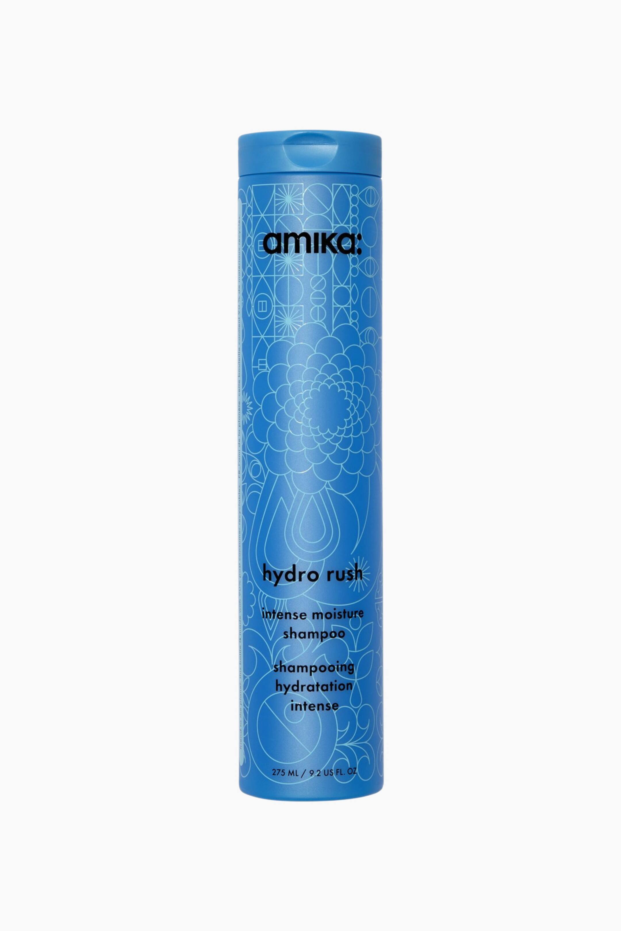 Visa större bild: En hög, cylindrisk blå flaska av amika Hydro Rush Intense Moisture Shampoo står upprätt och vänd framåt. Flaskan har intrikata ljusblå geometriska och blommiga linjemönster över hela ytan, med svart text som visar varumärket och produktnamnet.