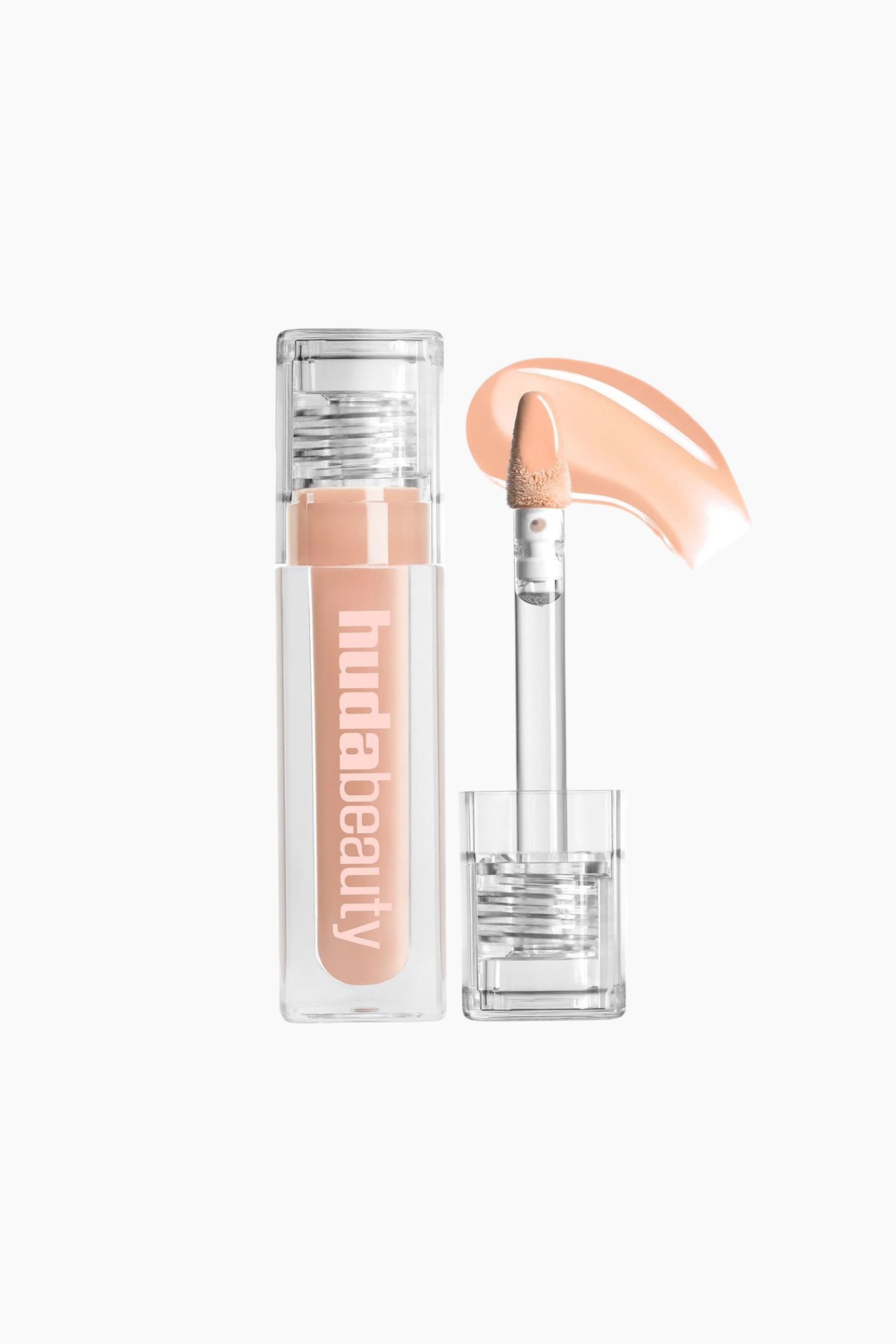 Visa större bild: En Huda Beauty flytande kosmetikprodukt presenteras i ett klart rektangulärt rör, fyllt med en ljus persikofärgad vätska och med "hudabeauty" vertikalt på sidan. Bredvid står en klar applikatorstav med en fotformad spets, belagd med samma persikofärgade vätska, upprätt, med ett matchande böjt prov av produkten bredvid.