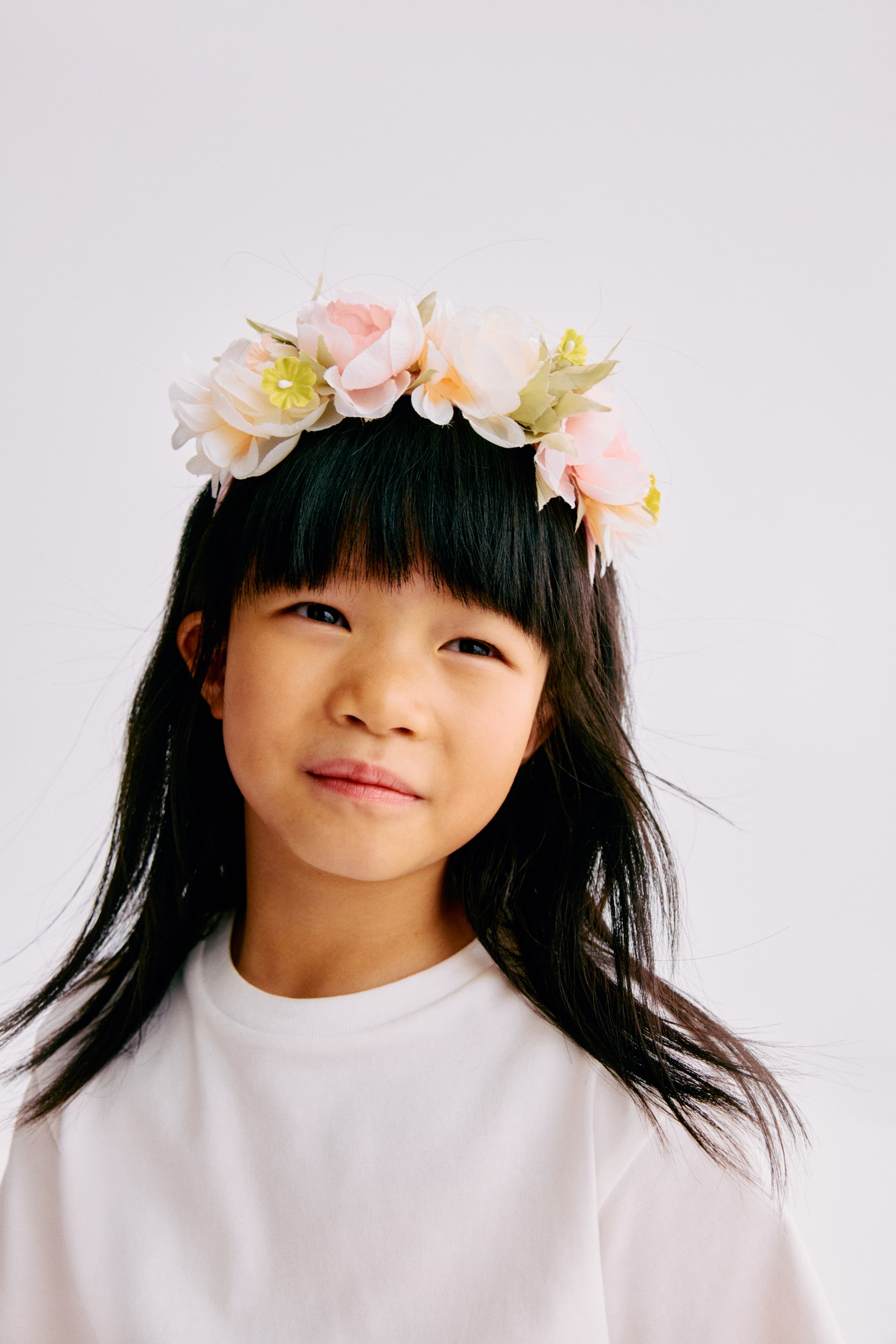 View larger image: A flower crown is resting on dark hair, encircling the head. It features light pink and cream fabric flowers with small yellow accents and green foliage.