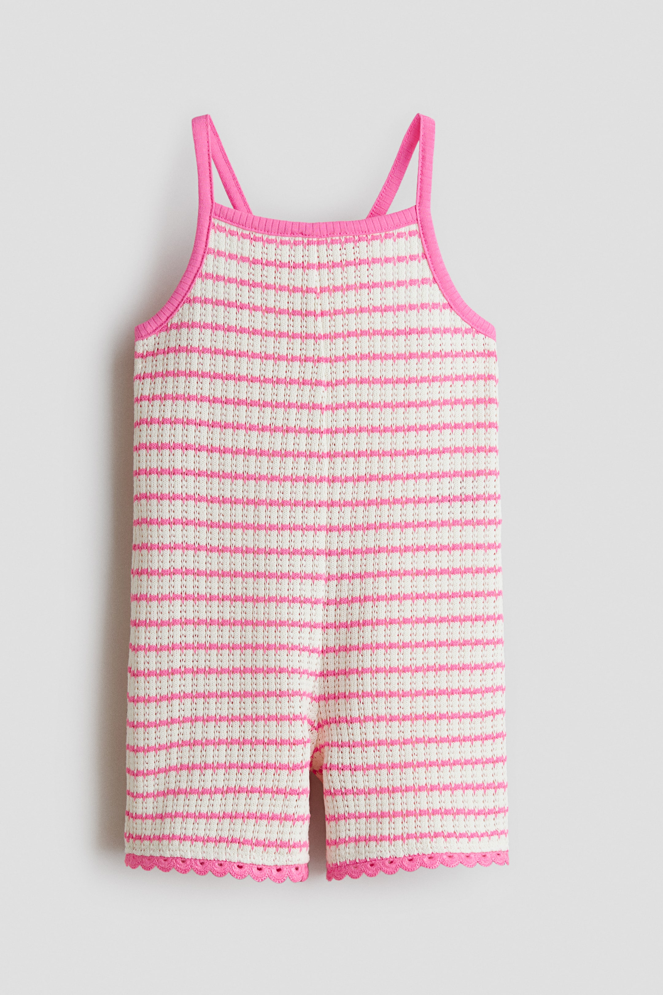 Grösseres Bild ansehen: Ein kurzer Jumpsuit präsentiert sich von vorne, aus weichem Pointelle-Strick in Weiss mit horizontalen rosa Streifen. Er ist mit einem quadratischen Ausschnitt, schmalen rosa Trägern und rosa Muschelsäumen gestaltet.
