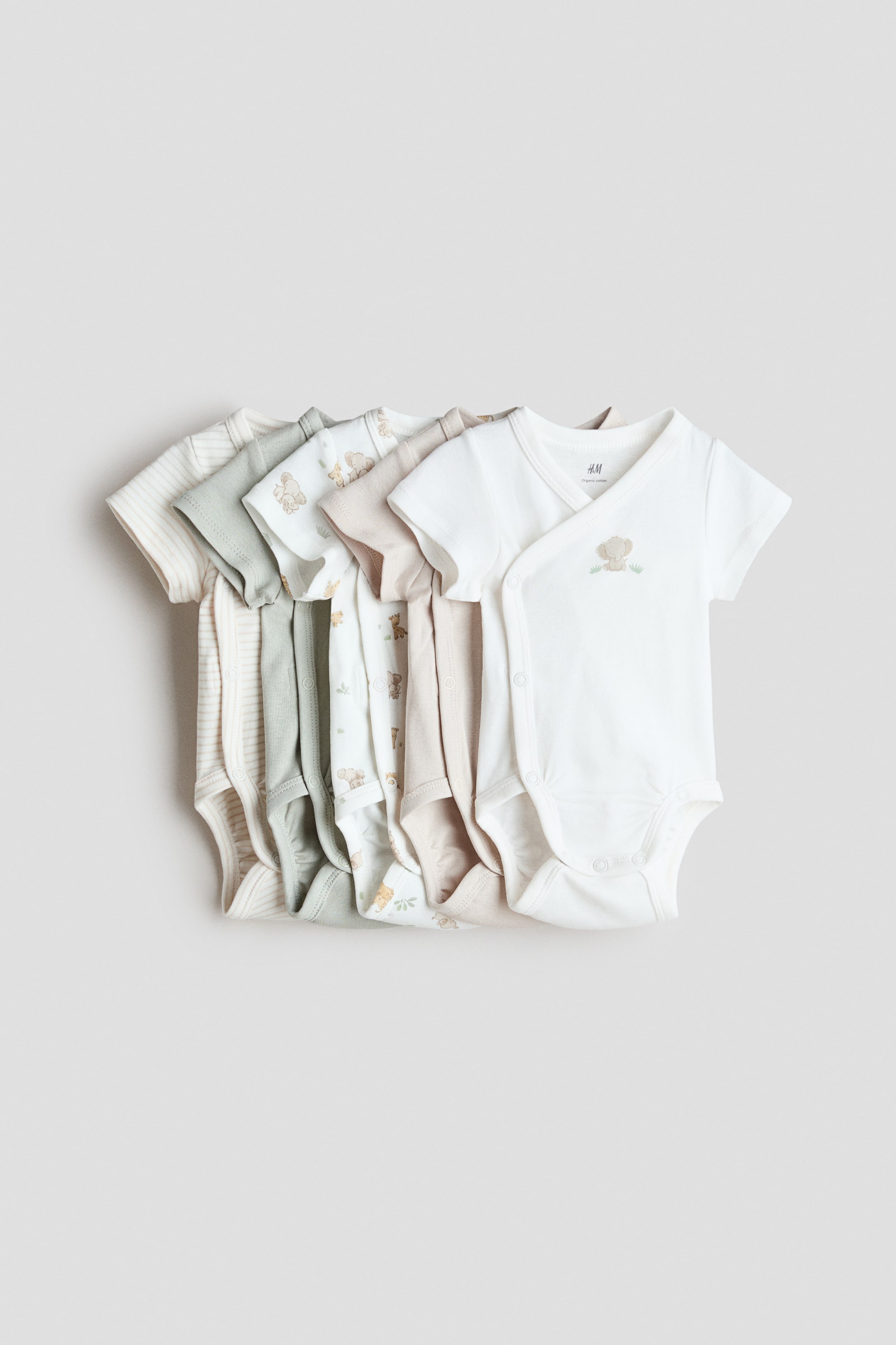 View larger image: A set of five short-sleeve bodysuits made from soft cotton jersey is shown from the front, highlighting a wrapover design with snap closures at the sides and crotch. The bodysuits come in white, light green, and beige, with some featuring subtle patterns like stripes or animal motifs.