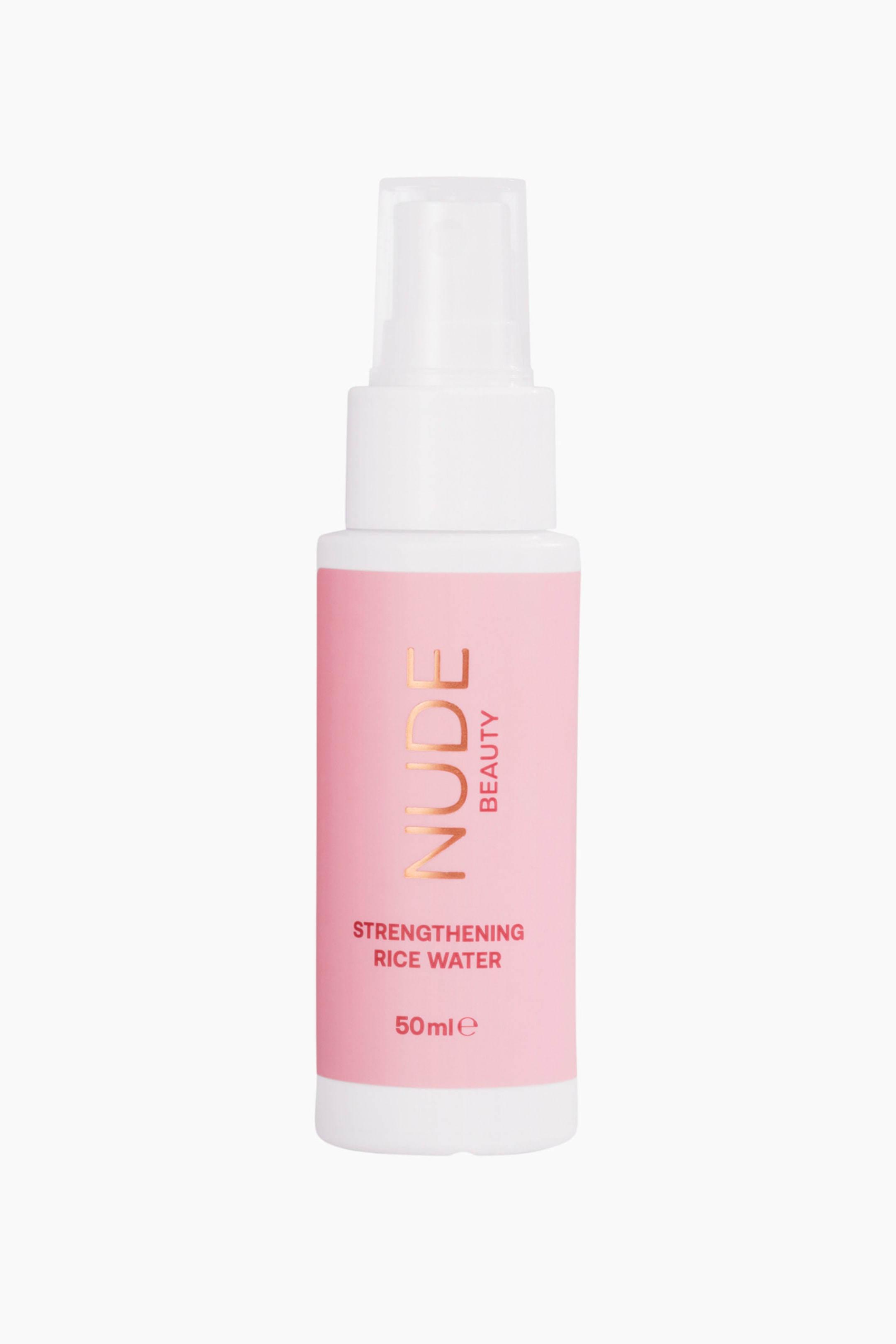 Vis større bilde: En hvit sprayflaske med en rosa etikett står oppreist, vendt fremover. Etiketten viser "NUDE BEAUTY" i gullbokstaver, og "STRENGTHENING RICE WATER 50ml e" i hvite bokstaver.