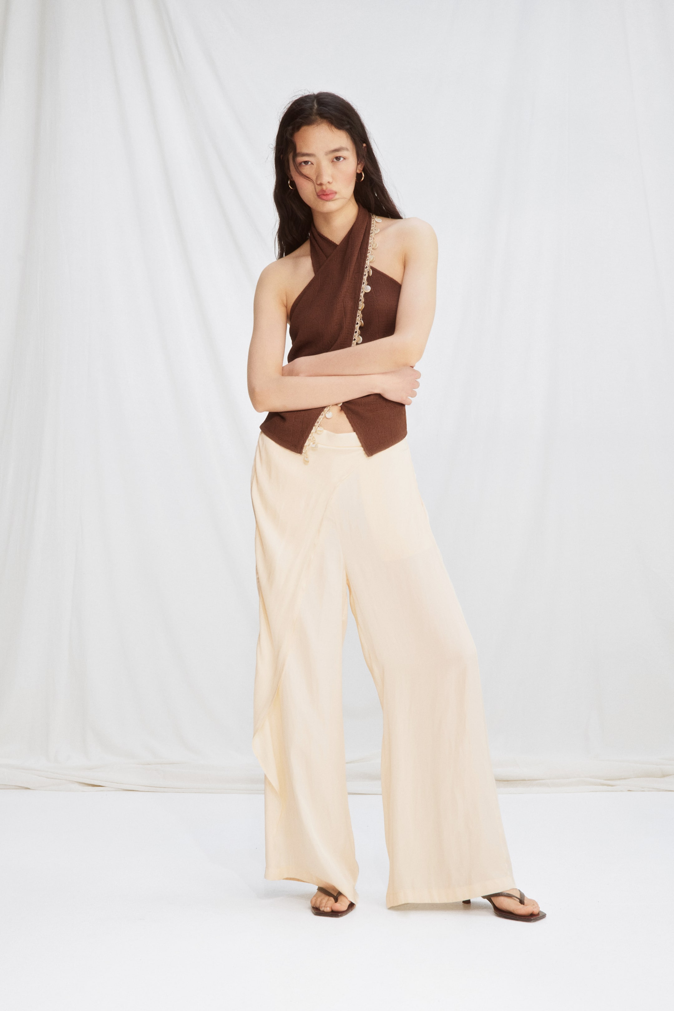 View larger image: "Wide-leg trousers in softly draping cream satin, featuring covered elastication at the back of the waist and a sewn-in wrap detail at the front, are being worn by the model."