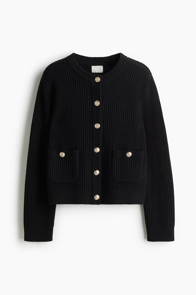 A short black cardigan is being displayed FRONT, showcasing a rib knit texture, a round neckline, and gold-coloured metal buttons running down its front. Two patch pockets, each adorned with a button, are visible on the lower front, while gently dropped shoulders and long sleeves are completing its design. - 1