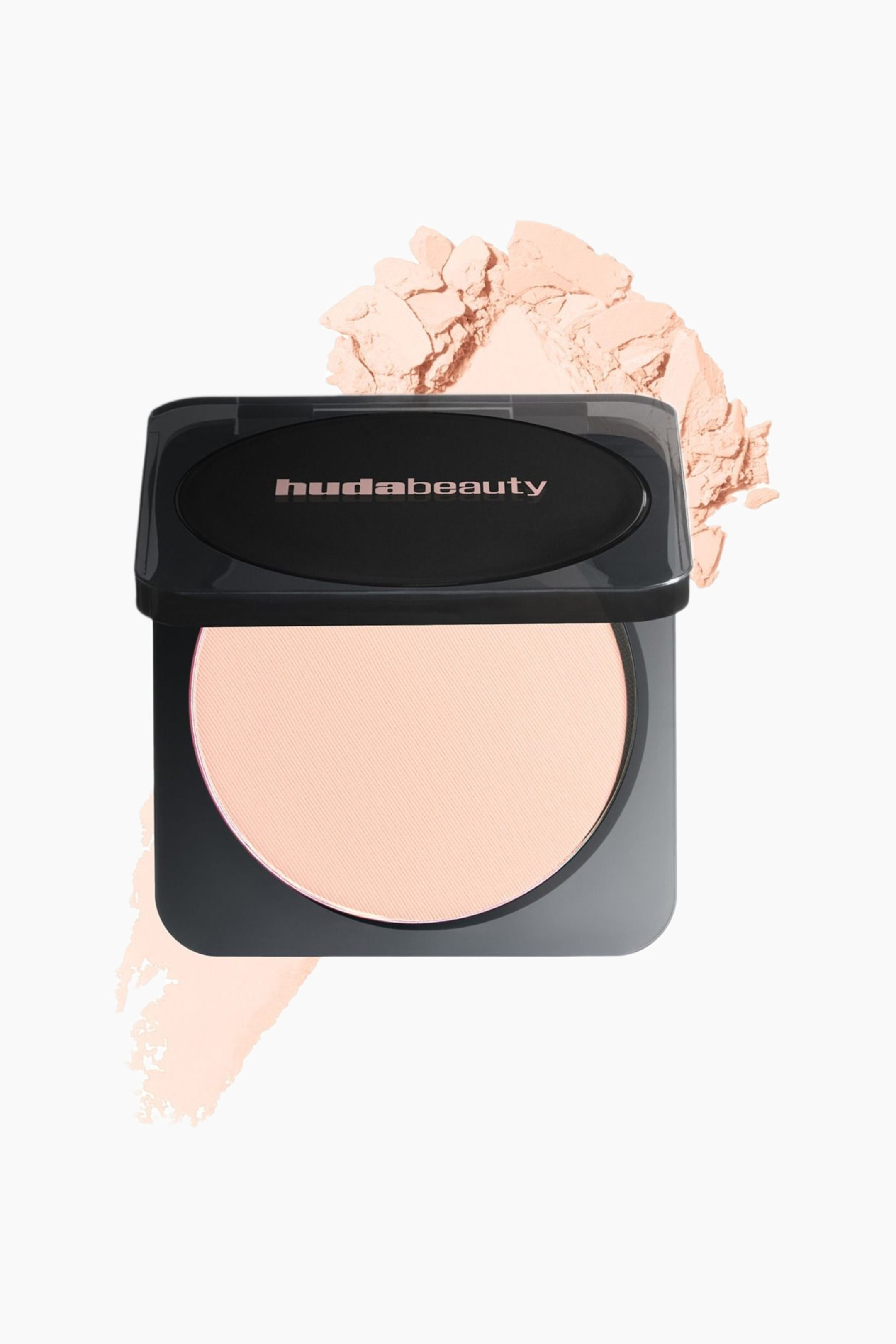 Näytä suurempi kuva: Avattu Huda Beautyn pressattu puuterikompakti on asetettu hieman oikealle kallistettuna, ja sen mustassa kotelossa näkyy vaalean persikka-beigen sävyinen pressattu puuteri. 'hudabeauty'-logo näkyy ruusukultaisin kirjaimin avatun kannen sisäpuolella, ja samaa irtopuuteria on ripoteltu tuotteen taakse.