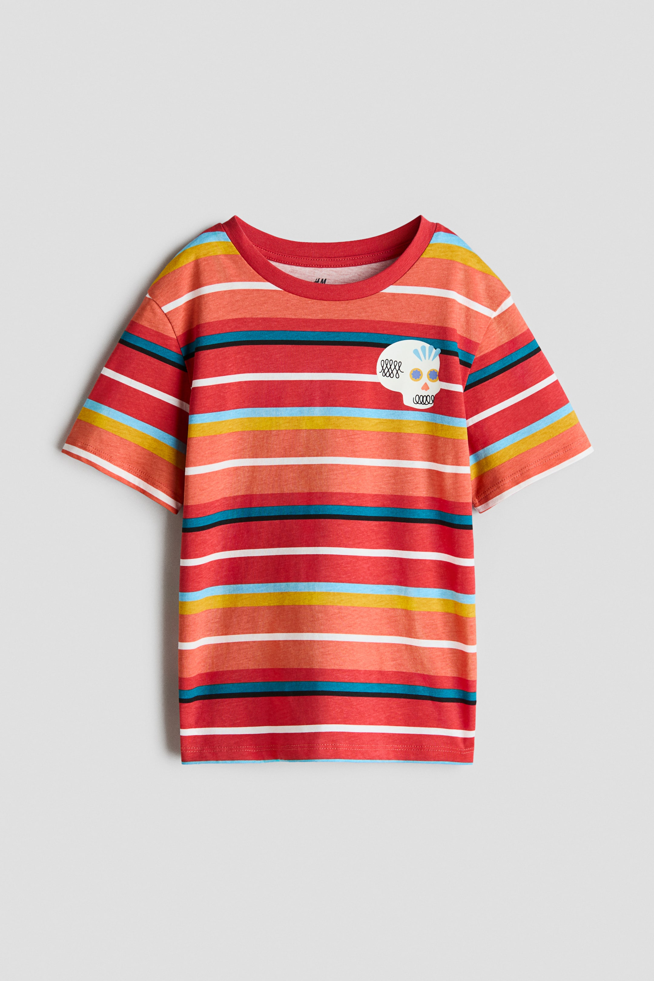 View larger image: The t-shirt is laid out flat, showcasing a multicolored horizontal stripe pattern in shades of red, orange, yellow, white, and teal. Crafted with a ribbed red crew neck and short sleeves, it features a white skull graphic with blue, yellow, and orange accents adorning the left chest.