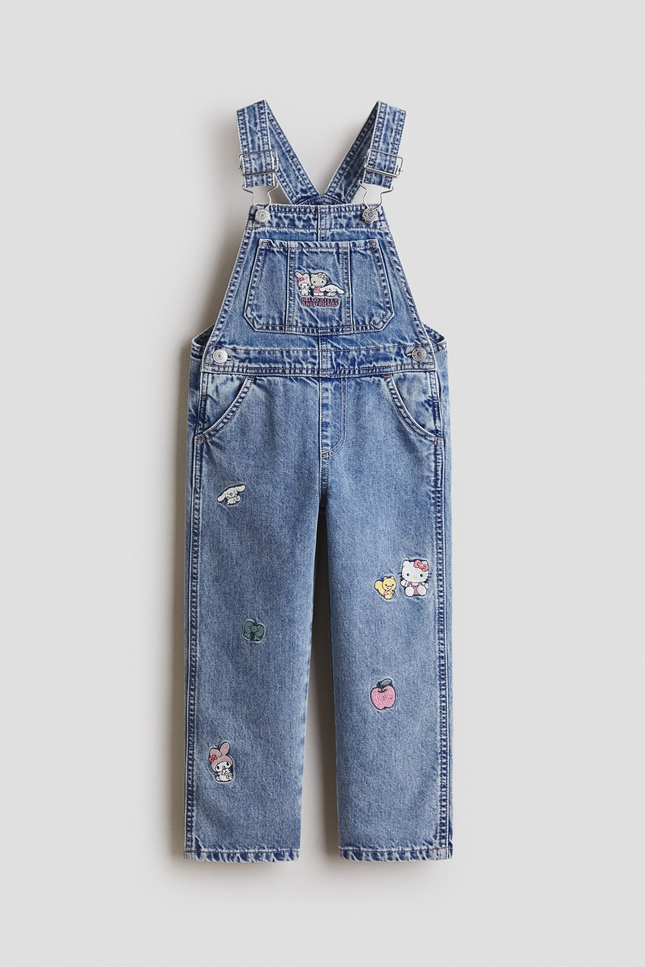 View larger image: Denim overalls are shown from the front, featuring a light blue wash and adjustable shoulder straps with silver-toned buckles. A bib pocket displays an embroidered "Hello Kitty and Friends" patch, while multiple Sanrio character patches, including Hello Kitty, My Melody, and Cinnamoroll, decorate the straight legs.