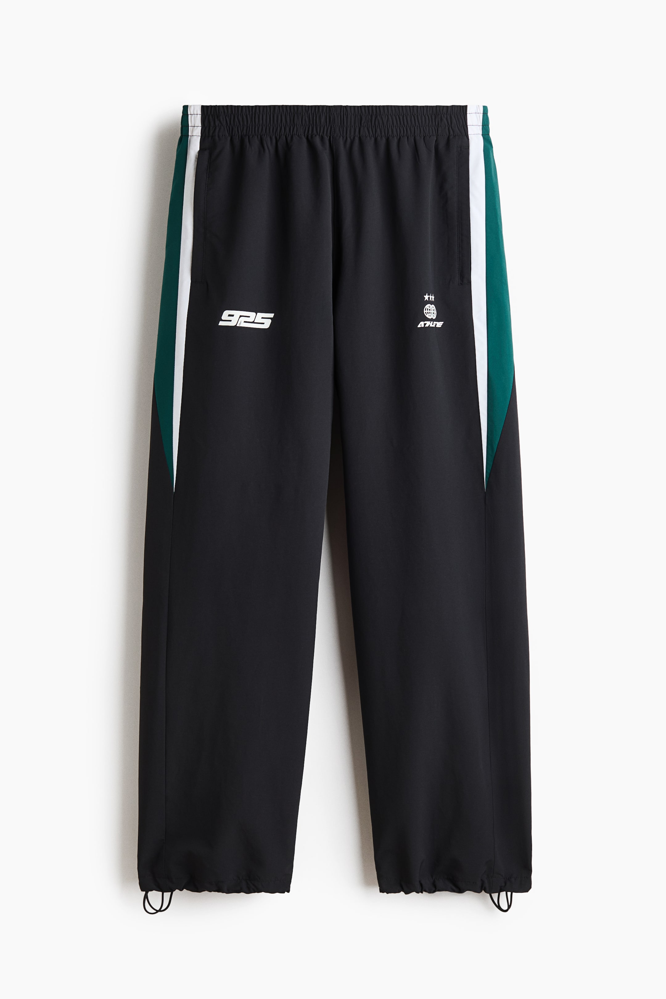 View larger image: A pair of black track pants is shown from the front, featuring an elastic waistband, side pockets, and adjustable bungee cord drawstrings at the hems. The pants feature green and white colour-blocked side panels, a white "925" graphic on the right leg, and a small white logo on the left leg.