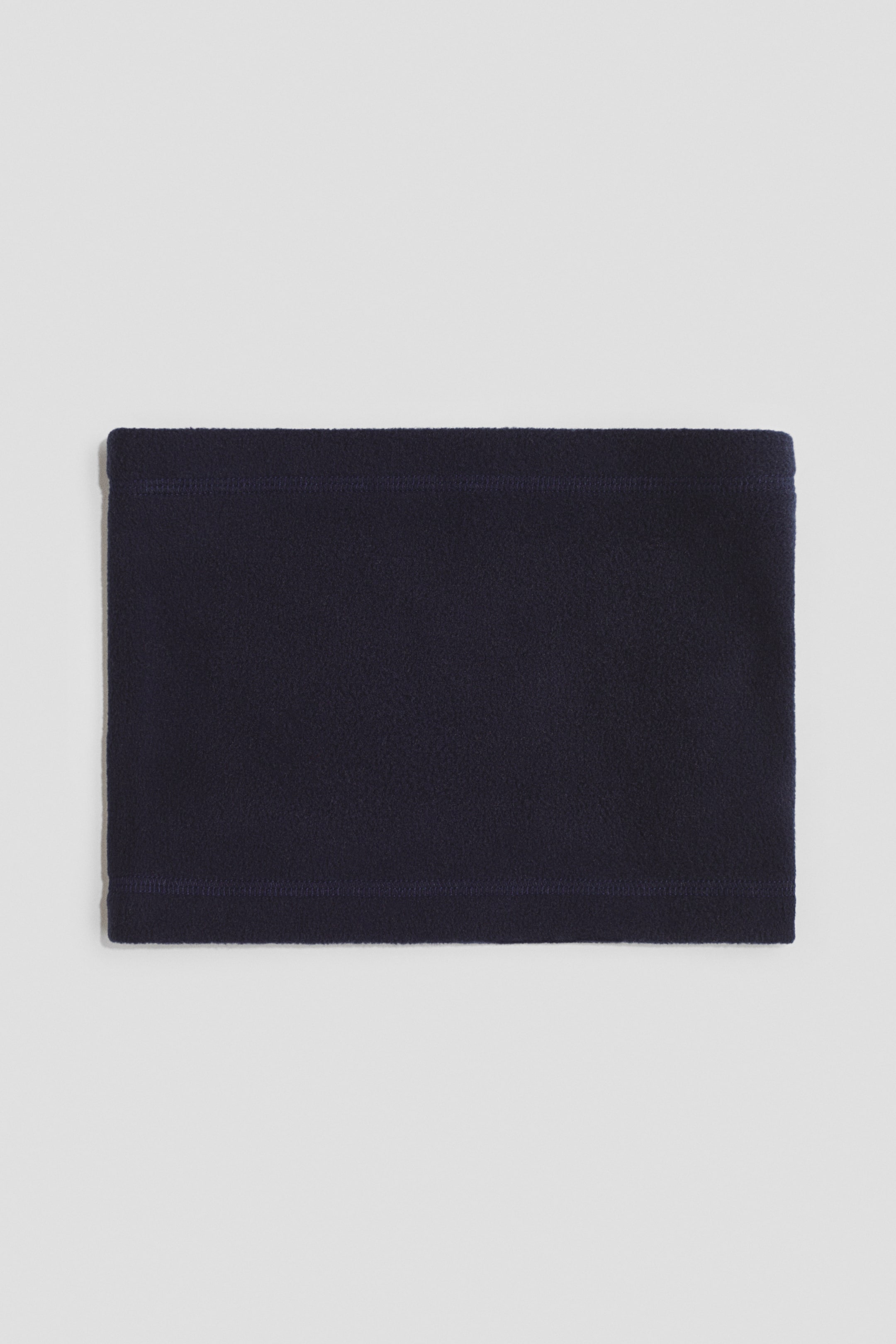 Größeres Bild ansehen: Ein dunkelblauer Fleece-Halswärmer wird flach präsentiert und zeigt seine weiche Textur. Entlang der oberen und unteren Kanten verlaufen horizontale Nähte.