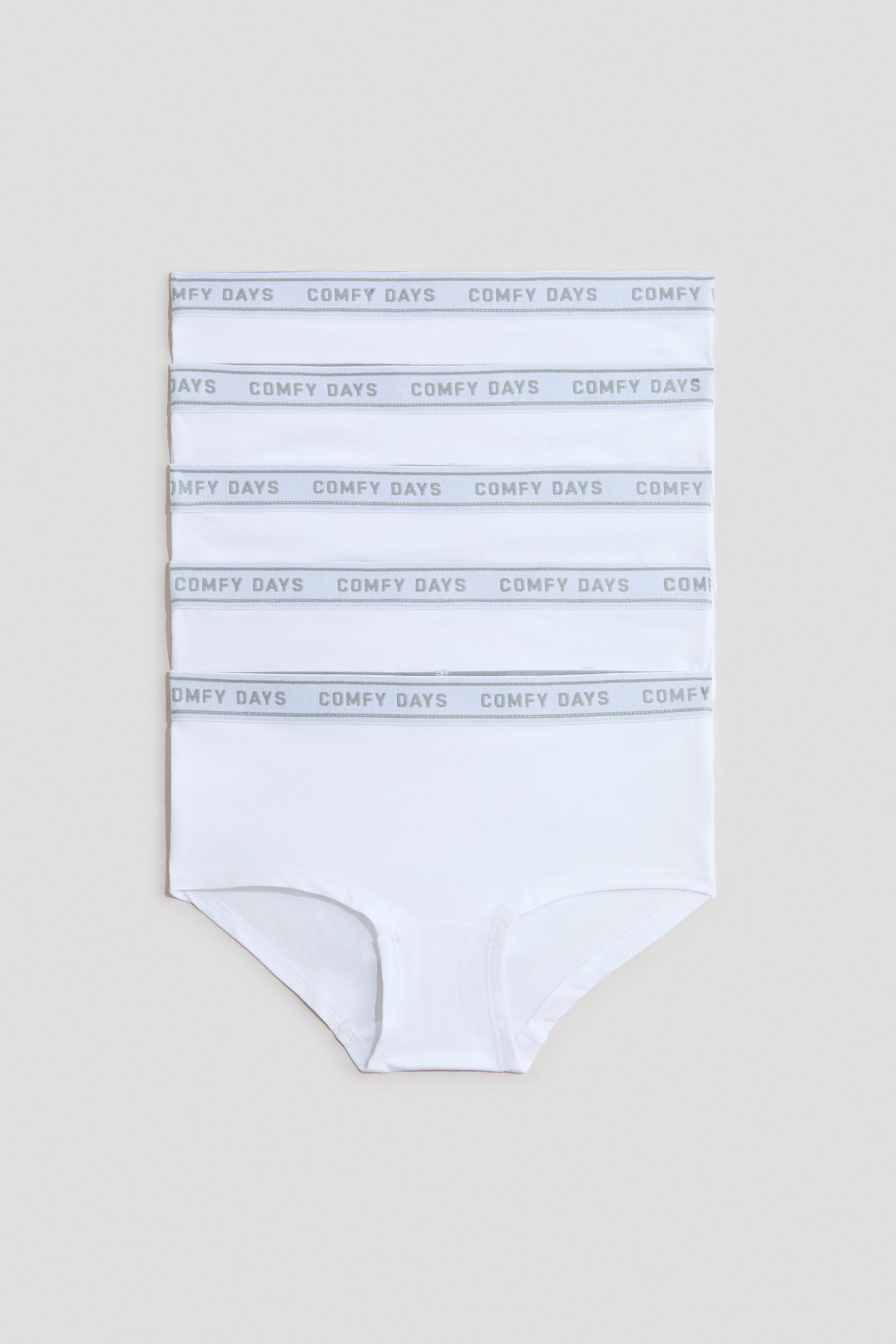 View larger image: Five white briefs are neatly stacked, each featuring a white elastic waistband with repeating grey text reading "COMFY DAYS" and presenting a front-facing view.
