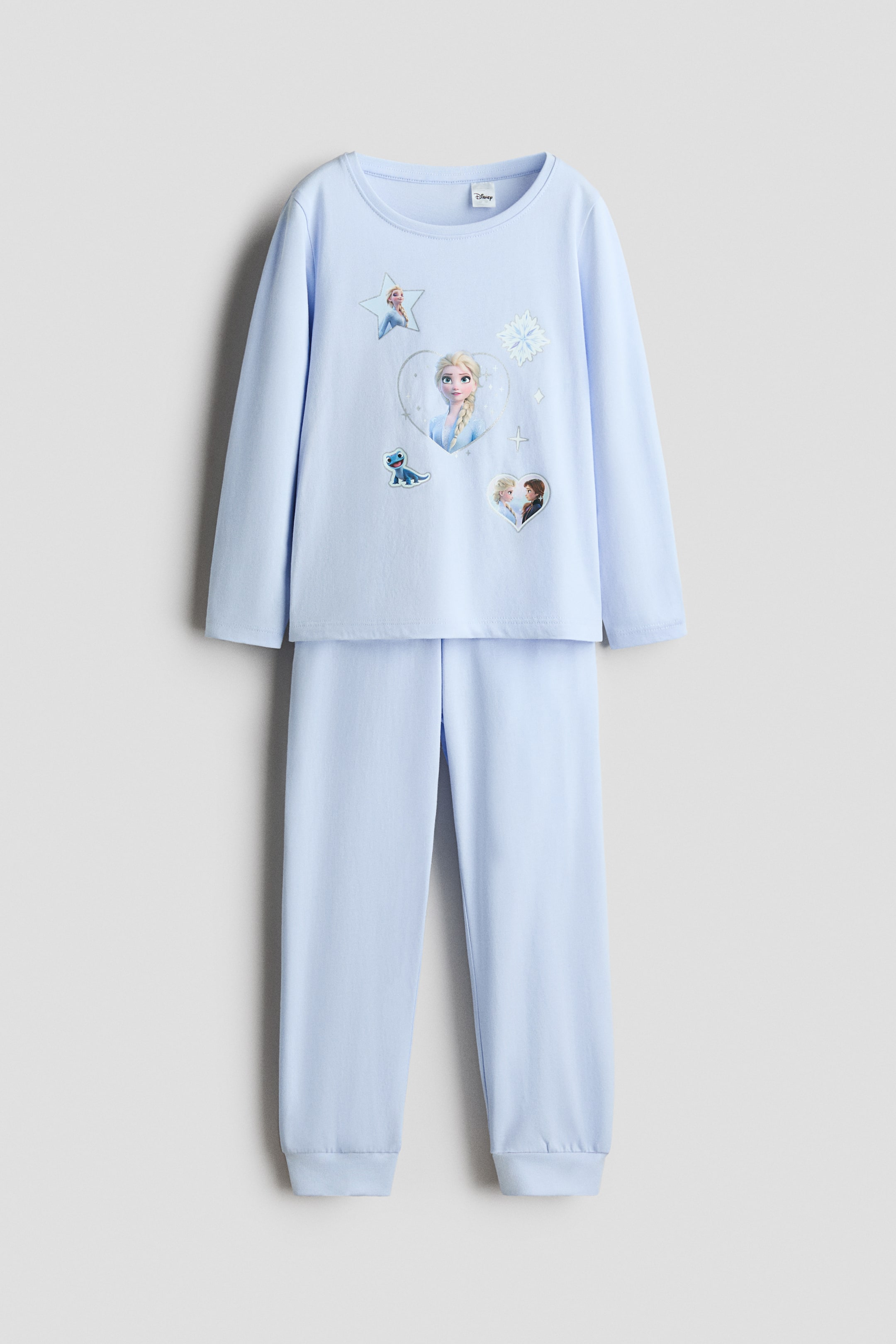 View larger image: Light blue soft cotton jersey pyjamas are presented from the front. The top features a round neckline, long sleeves with ribbed cuffs, and a graphic print depicting Elsa in a central heart, surrounded by smaller images of Elsa in a star, a blue lizard character, and Elsa with Anna in a heart, along with snowflake motifs, while the matching bottoms feature an elasticated waist and ribbed hems.