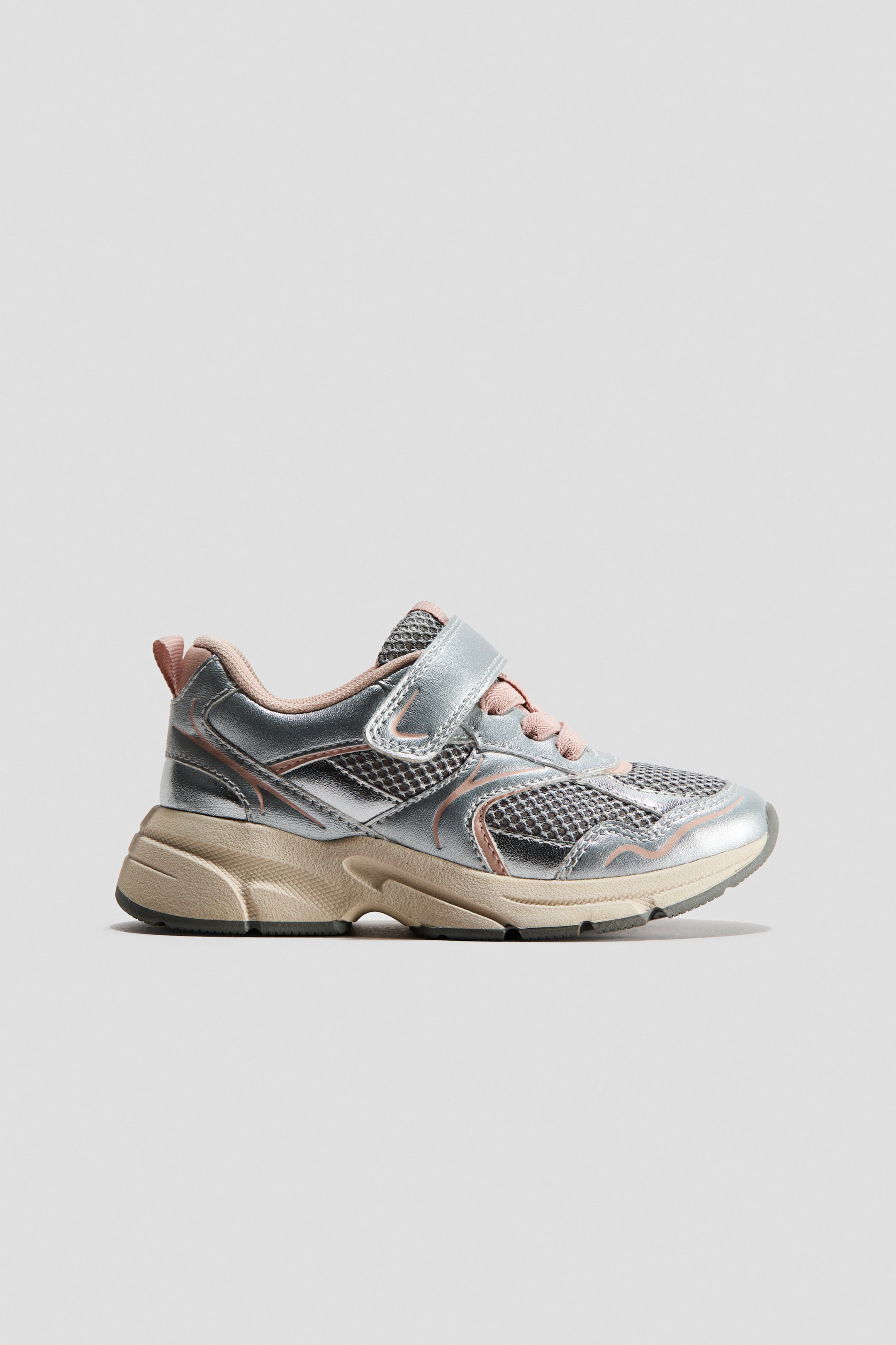 View larger image: A silver and pink sneaker is showcased in a side view, highlighting metallic silver panels, gray mesh sections, and pink trim details. A single pink hook-and-loop strap secures the shoe over pink laces, and a chunky beige and gray sole supports the design.