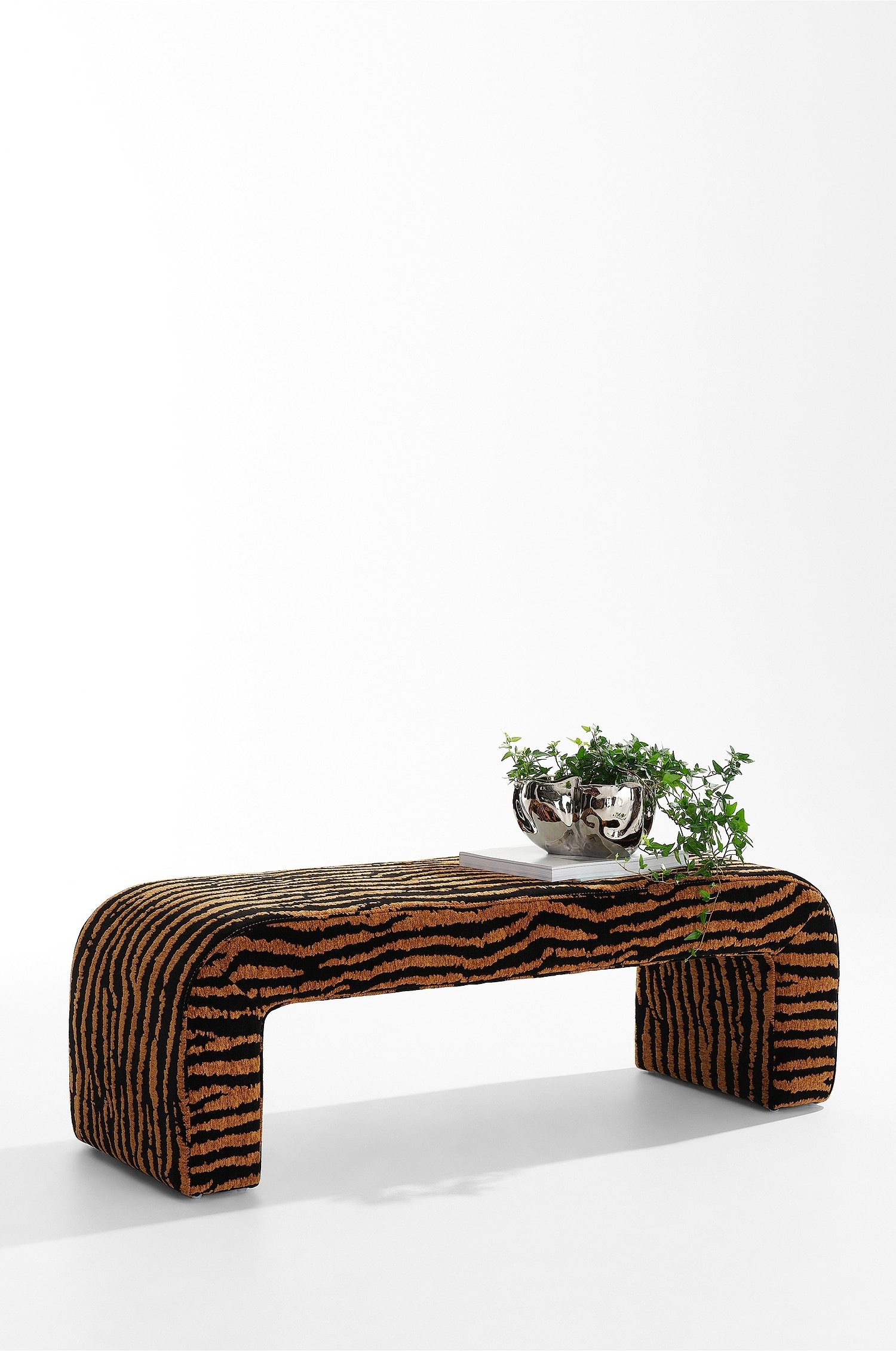La panca Odette è in piedi con unâangolazione di tre quarti, mettendo in risalto un design continuo e curvo a cascata. à rivestita in un tessuto testurizzato con motivo zebra nero e marrone che ricopre lâintera struttura a U.