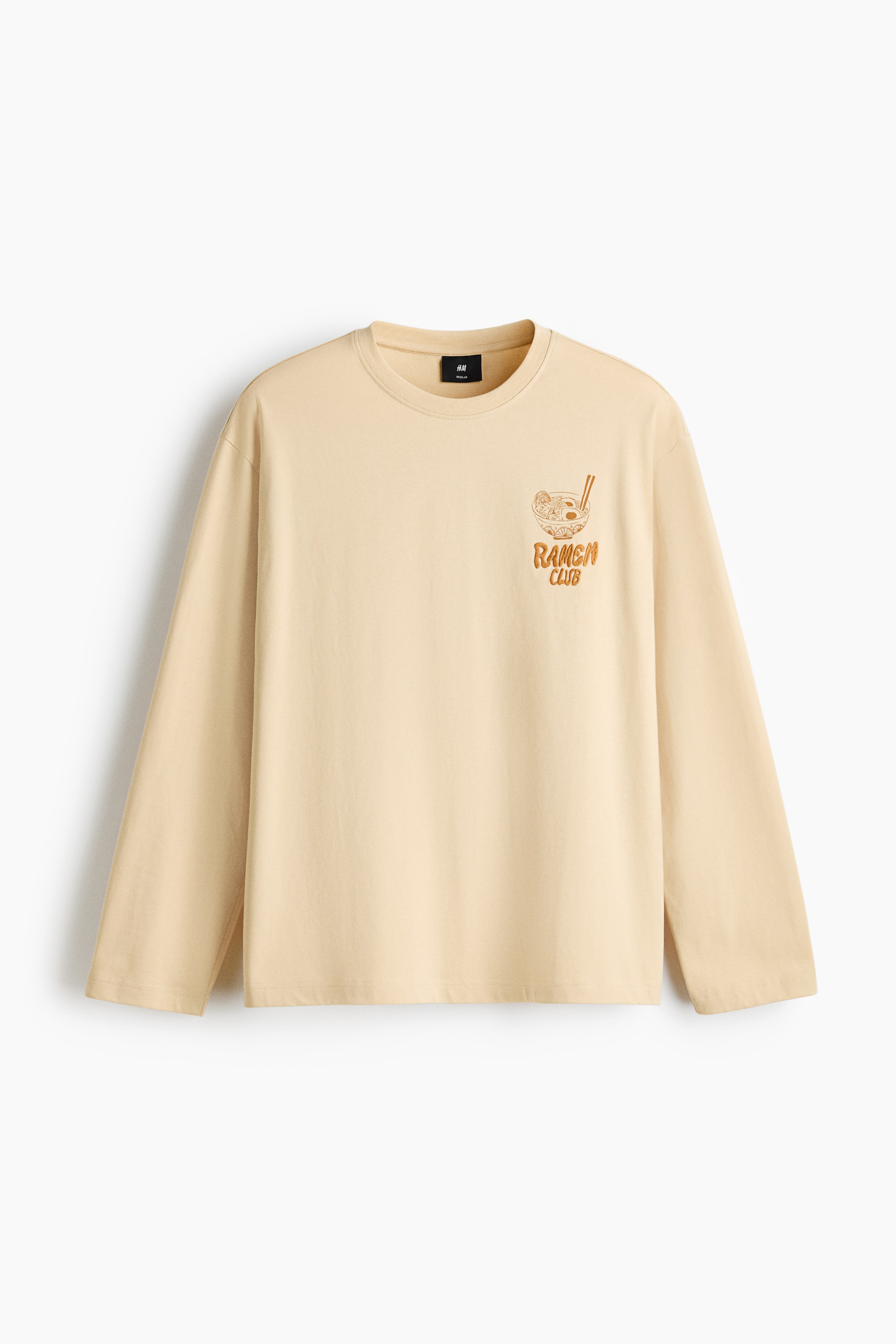 View larger image: A light beige long-sleeved T-shirt features a crew neck and loose-fitting sleeves, with the front facing forward. A graphic of a ramen bowl with chopsticks and the text "RAMEN CLUB" in a darker orange colour appears on the left chest.