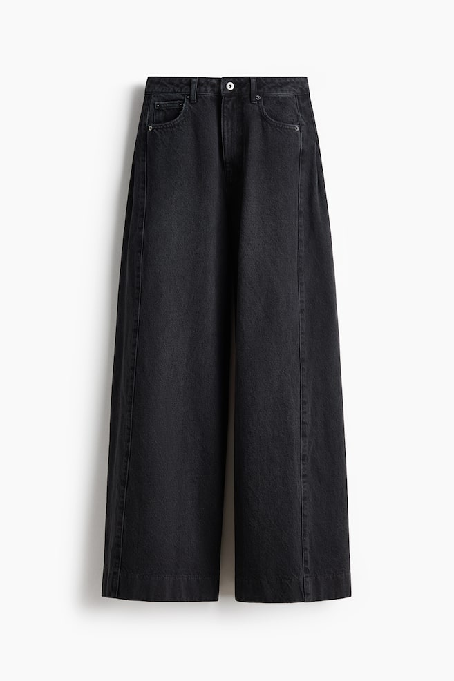 Black wide-leg jeans are displayed flat, showcasing a front view. They feature a high waist with a single button closure, belt loops, and two rounded front pockets. Distinct vertical seams run down the center front of each leg, extending to the wide, straight hem. - 1