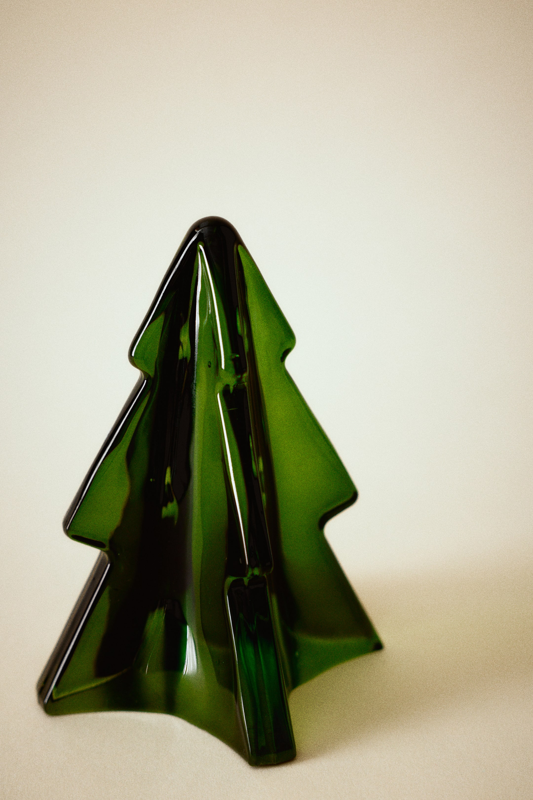 Visualizza l'immagine ingrandita: Una piccola decorazione in vetro a forma di albero di pino è in piedi rivolta in avanti, con un design stilizzato e tridimensionale, caratterizzato da rami angolari disposti a più livelli. La decorazione presenta una finitura verde lucida e traslucida, che crea diverse profondità di colore e riflette la luce sulle sue superfici lisce.