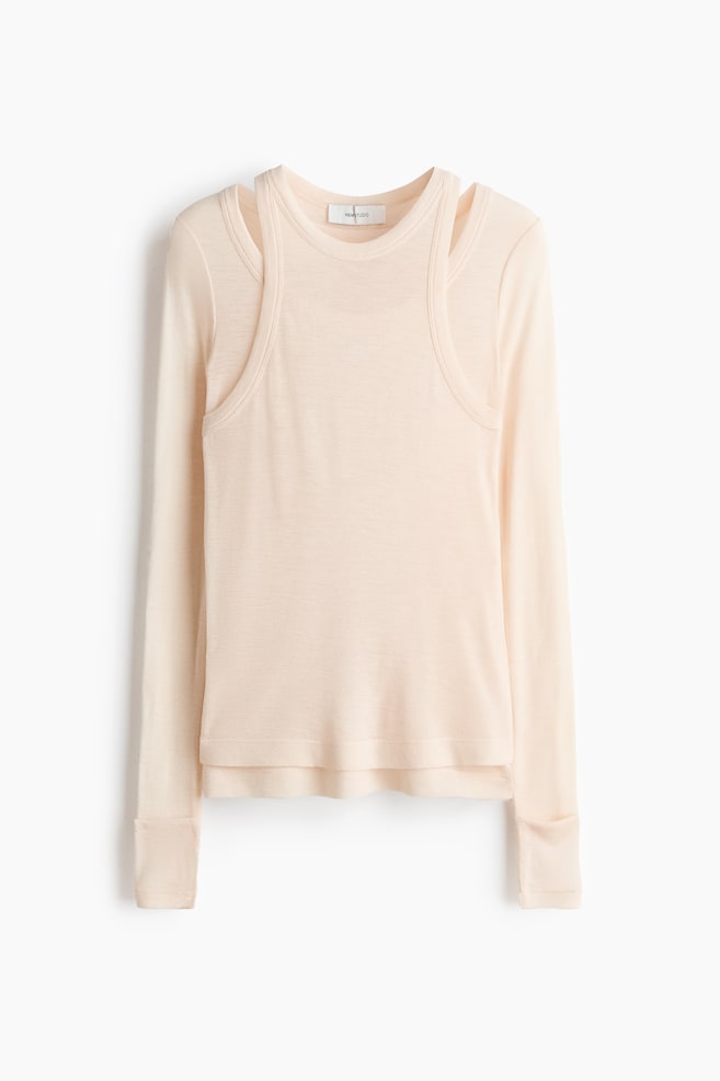 Ein blasses pfirsichfarbenes Langarmshirt mit Rundhalsausschnitt und integriertem Tanktop-Overlay im Scoop-Stil, das markante Cut-Outs an den Schultern schafft. Die langen Ärmel enden in umgeschlagenen Manschetten. - 1
