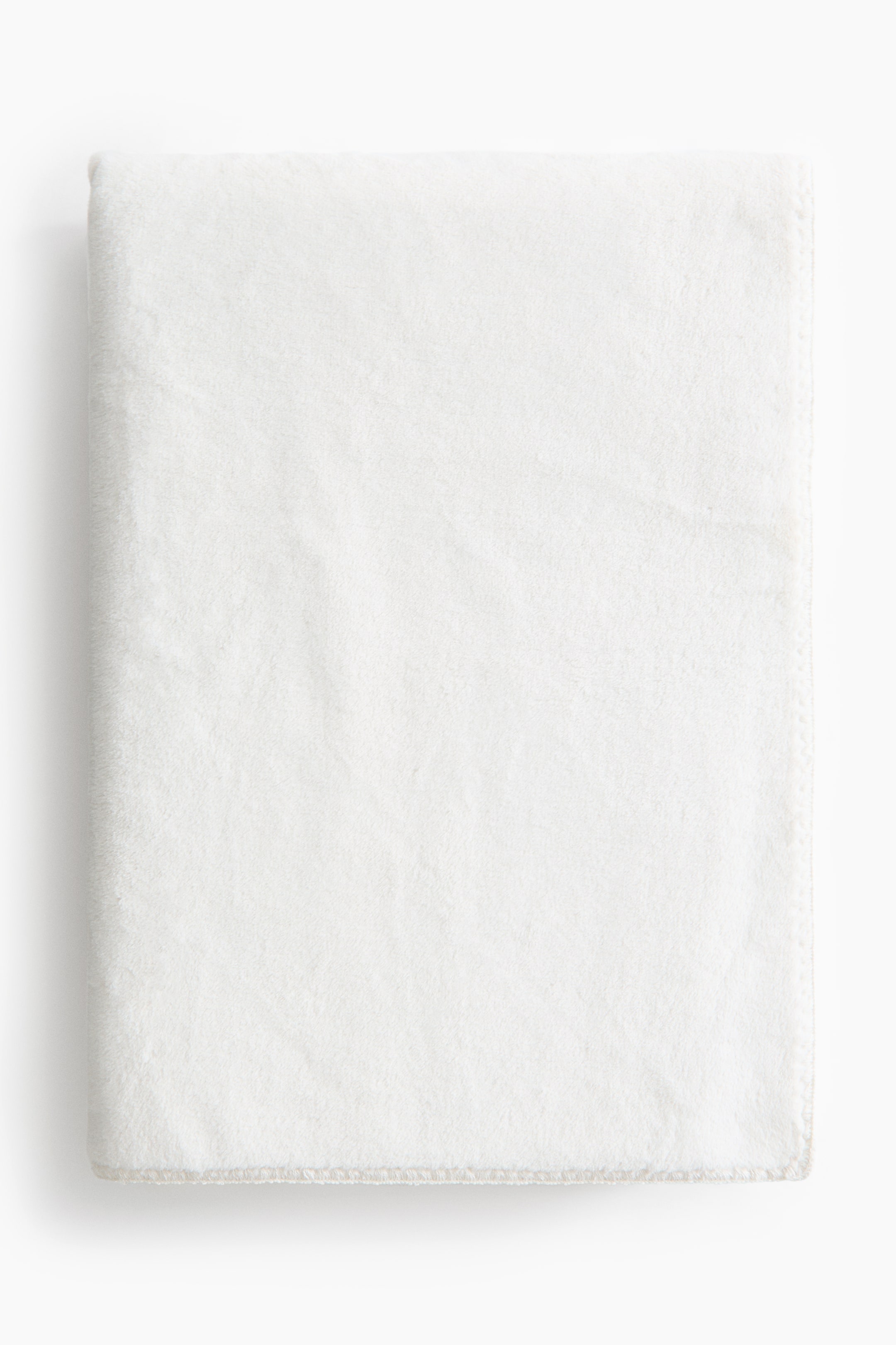 View larger image: A soft pile fleece throw blanket in off-white is lying neatly folded in a rectangular shape, displaying its velvety texture and a whipstitched bottom hem.