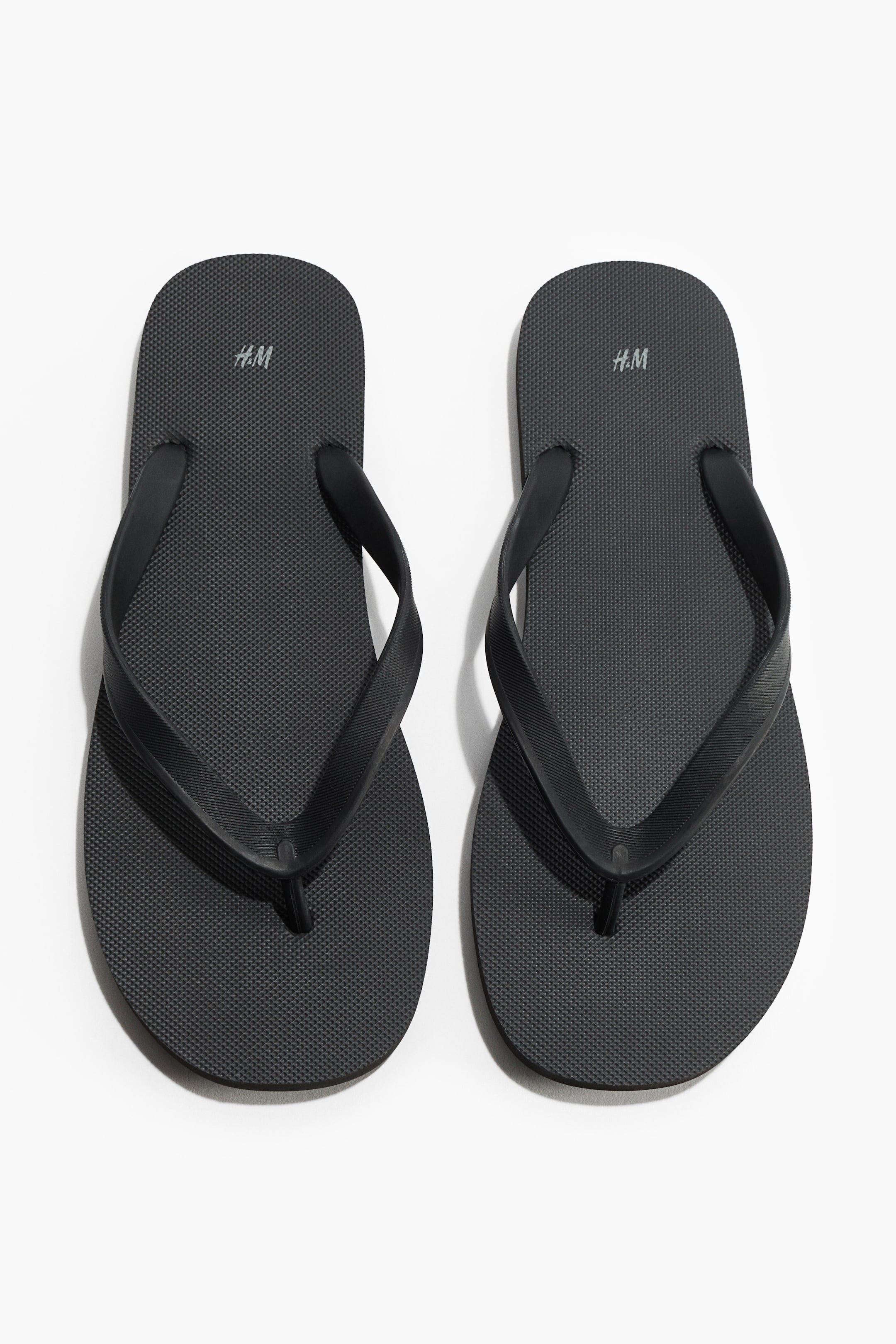 Größeres Bild ansehen: Ein Paar schwarze Gummi-Flip-Flops mit strukturierten Sohlen, breiten V-förmigen Riemen und einem schmalen Zehensteg. Sie sind frontal ausgerichtet dargestellt.