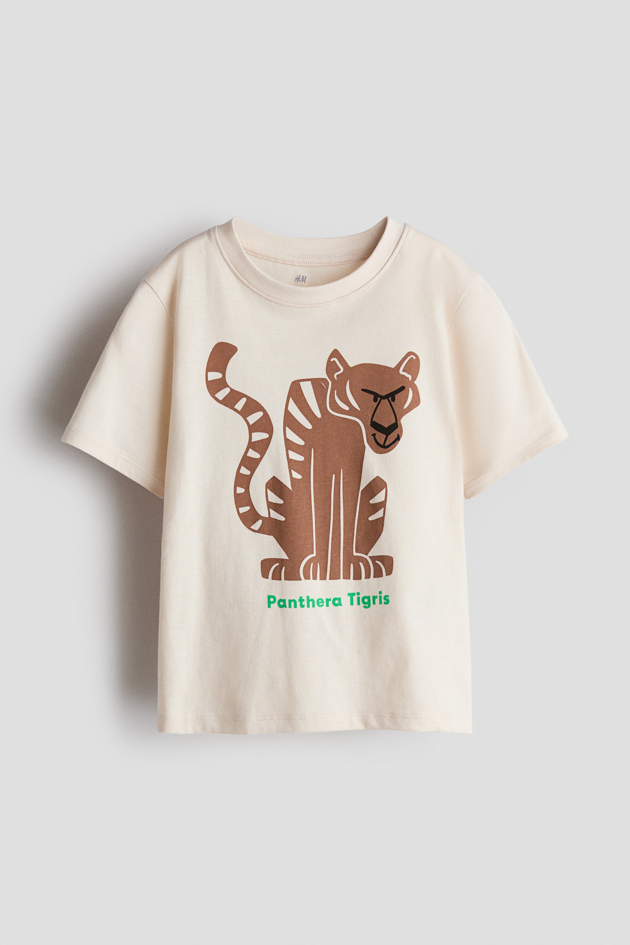 View larger image: A cream-colored, printed jersey T-shirt is displaying its FRONT, featuring a round neckline, short sleeves, and a brown graphic print of a sitting tiger with the green text "Panthera Tigris" beneath it.