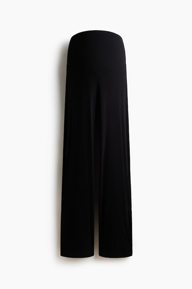 Black pants are presenting with a wide, ribbed high-rise waistband featuring a V-shaped seam at the front, and are flowing into wide legs. - 1