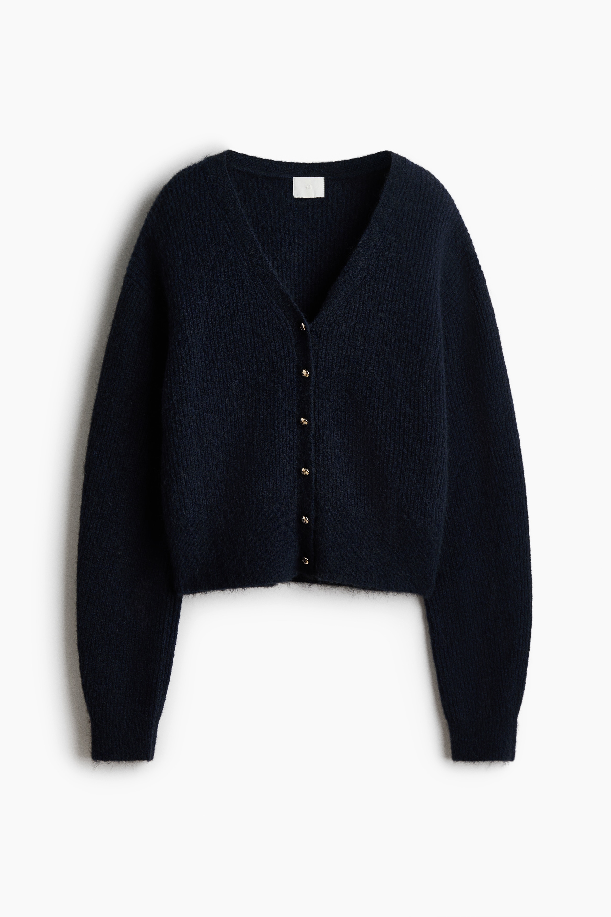 A dark, soft-knit cardigan is shown from the front, featuring a deep V-shaped neckline and a button-down front with a small gold button. The cardigan is layered over a light-coloured, lace-trimmed camisole, highlighting the relaxed fit and soft texture of the knit.