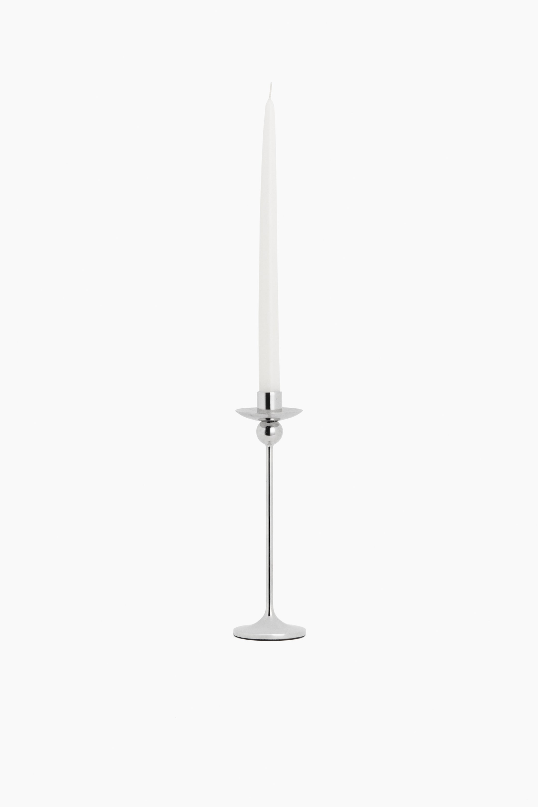 View larger image: A polished silver-toned metal candlestick holds a slender white tapered candle, featuring a round flat base, a thin stem with a small spherical detail, and a flared cup-shaped holder.