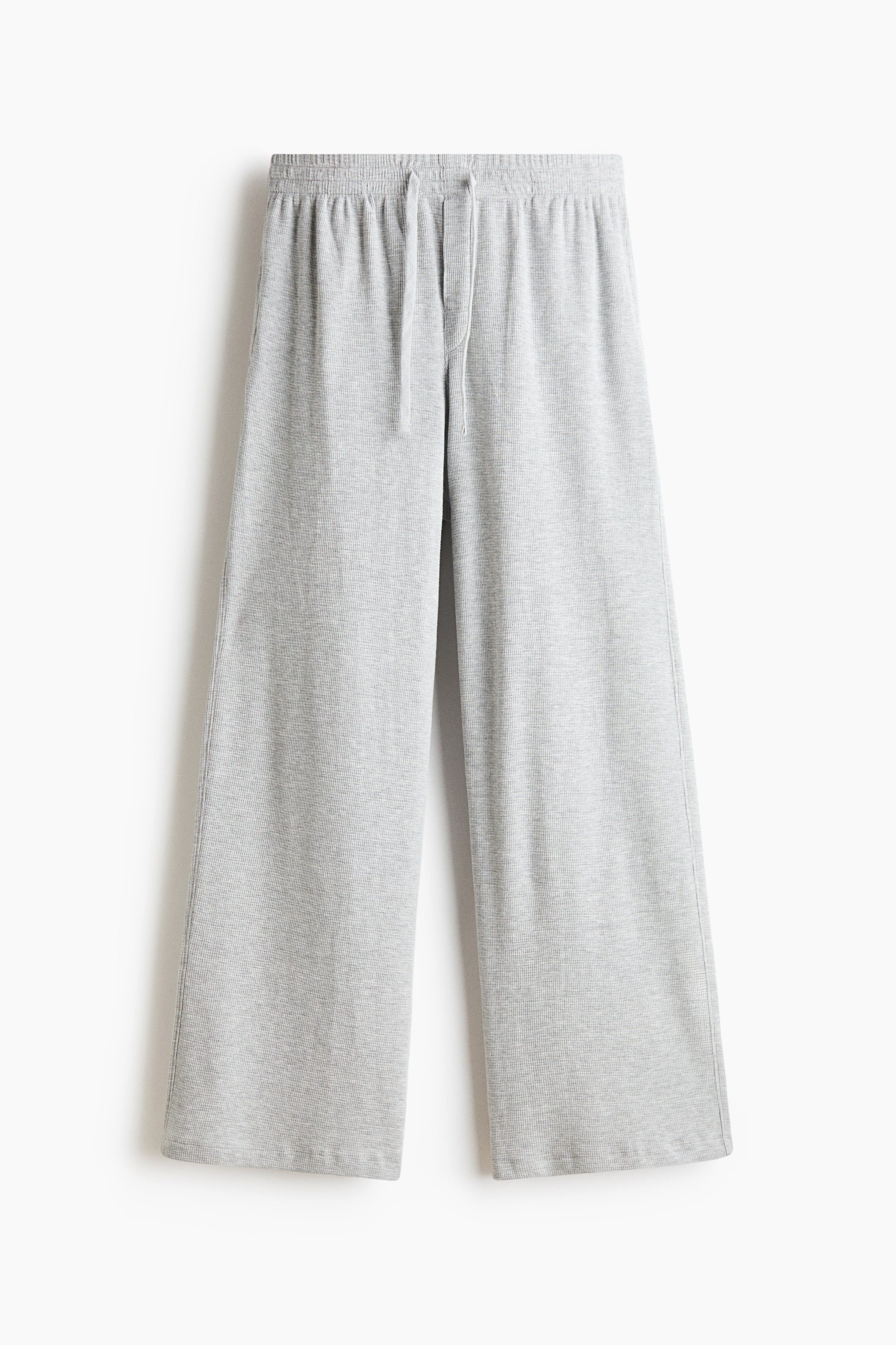 Grotere afbeelding bekijken: Een lichtgrijze broek met wijde pijpen wordt van voren getoond, met een elastische tailleband en een verstelbaar bijpassend trekkoord. De broek valt losjes en recht naar brede zomen, waardoor het zachte, getextureerde knitmateriaal mooi naar voren komt.