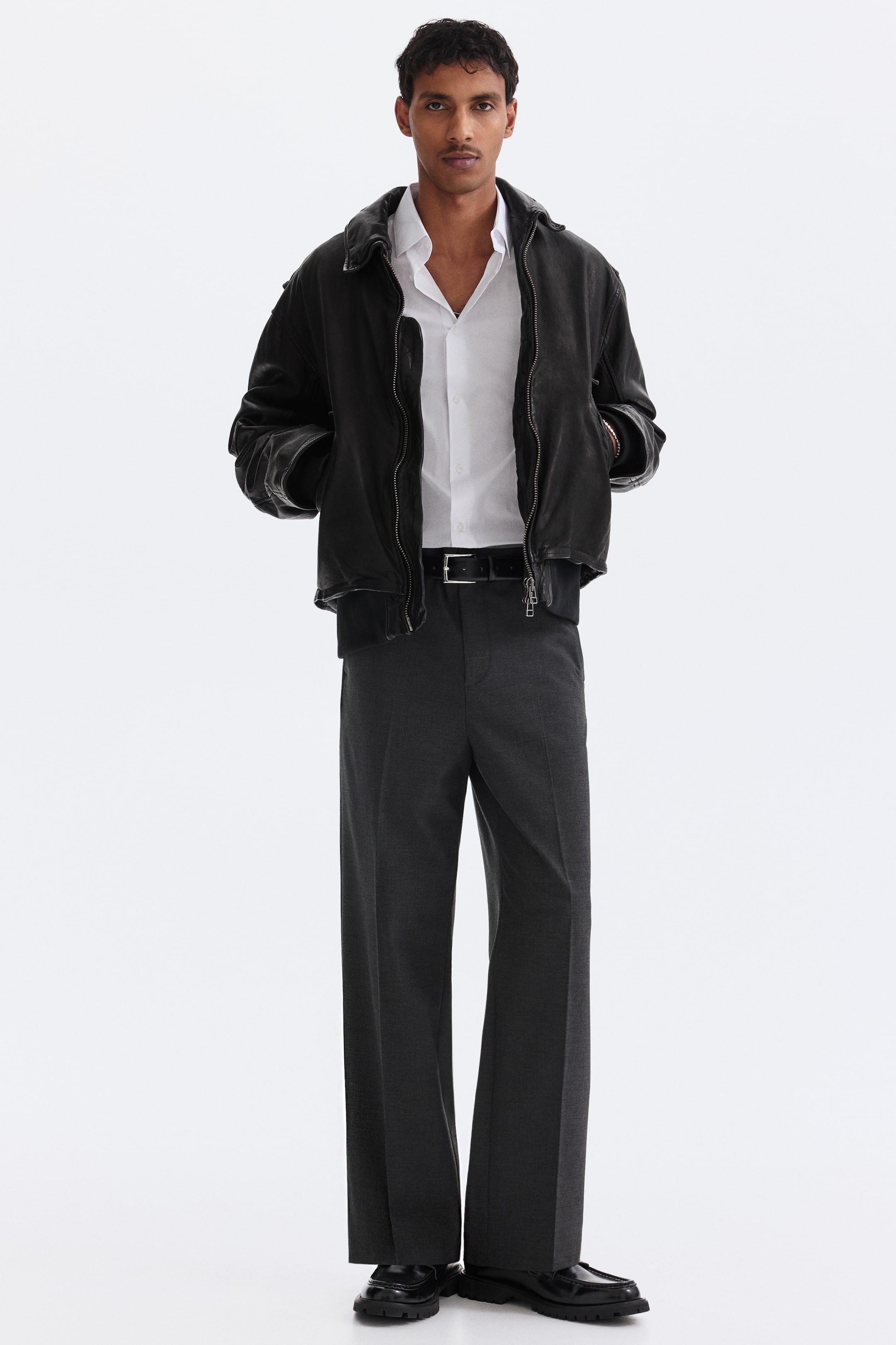 Voir une image plus grande: La veste bomber noire présente une texture noire mate et une coupe décontractée, avec un col classique, une fermeture éclair frontale et des poignets et un ourlet côtelés. Elle est portée ouverte par‑dessus une chemise blanche à col.