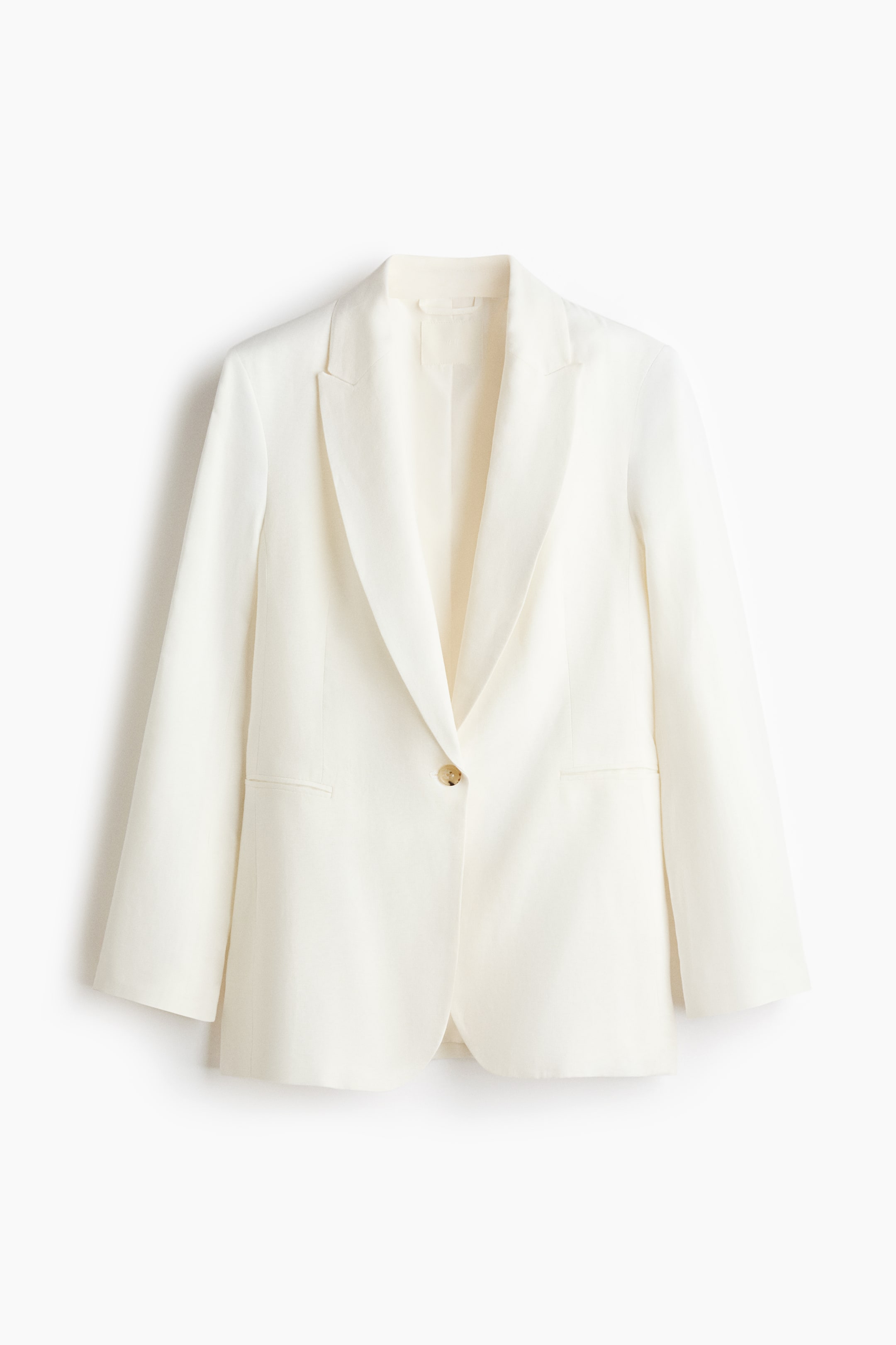 Grotere afbeelding bekijken: Een off-white enkelrij blazer toont zijn vooraanzicht en laat een geweven stoftextuur zien. Het heeft gepiekte revers, jetted voorzakken en een enkele lichtgekleurde knoopsluiting.