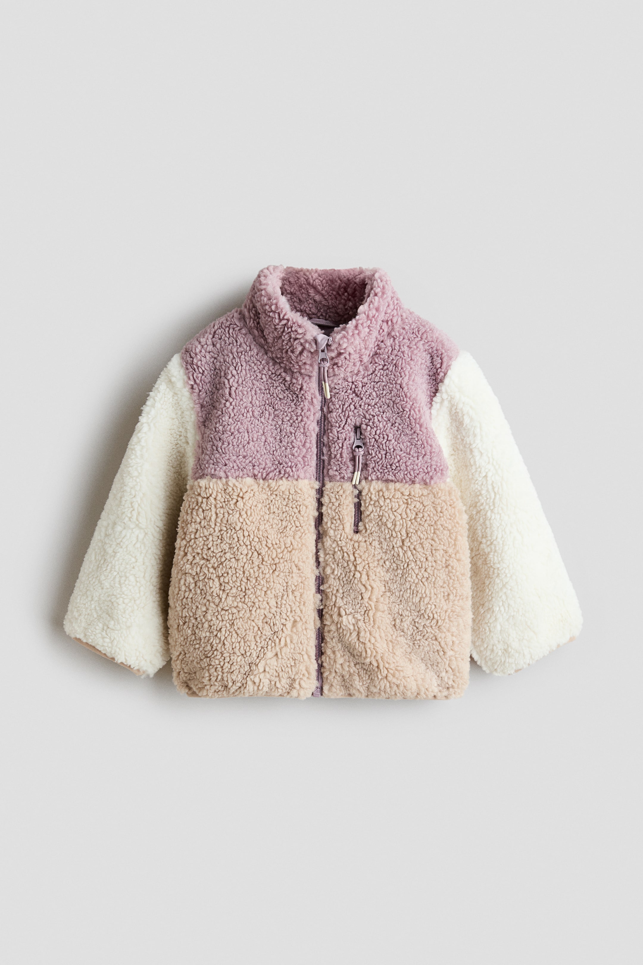 View larger image: A colour-block fleece jacket is featured at the front, boasting a stand-up collar. The jacket highlights a lilac top panel, a beige bottom panel, and cream sleeves, all in a sherpa texture, with a full-length lilac zip running down the front and a single lilac zippered chest pocket visible on the left side.