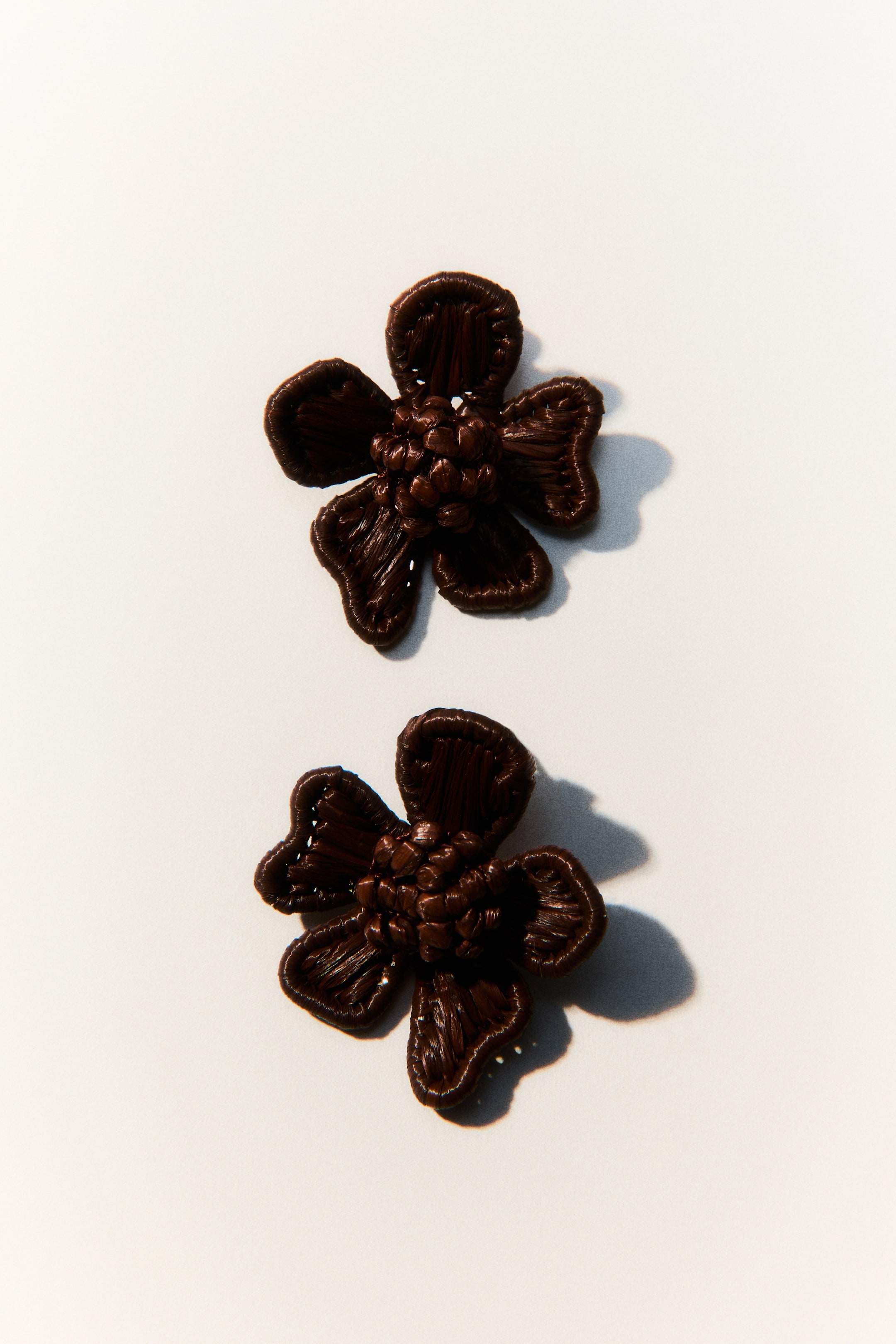 View larger image: "Two dark brown, flower-shaped items each showcase five textured petals, boasting a woven design across the petals and a densely clustered texture at their cores."