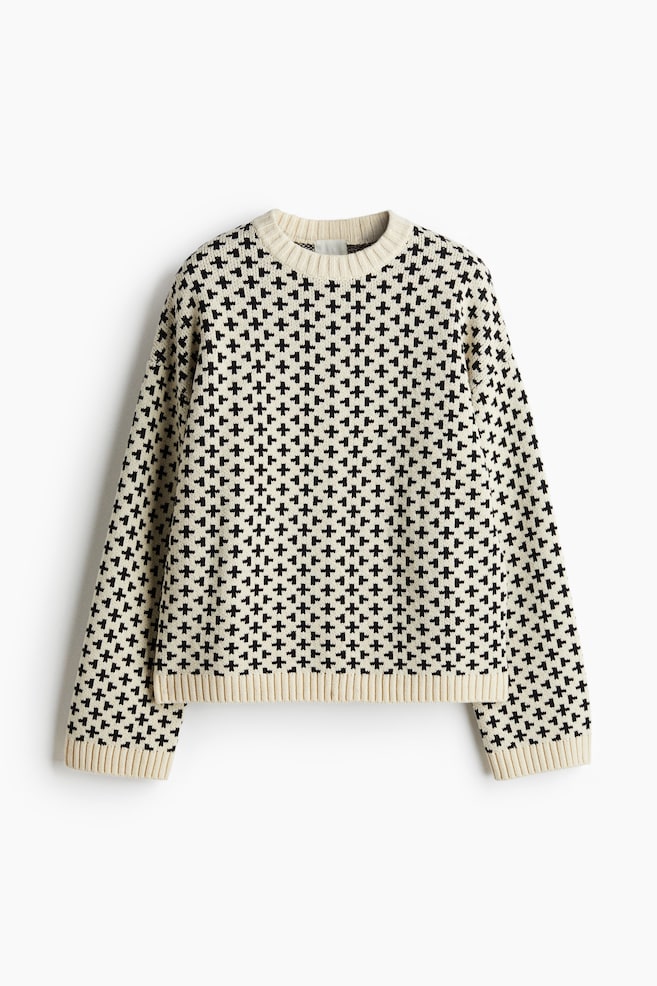 A sweater is displaying its front, featuring a cream and black geometric pattern of small crosses. It is designed with a crew neck, long sleeves, and is finished with ribbed cuffs and a ribbed hem. - 1