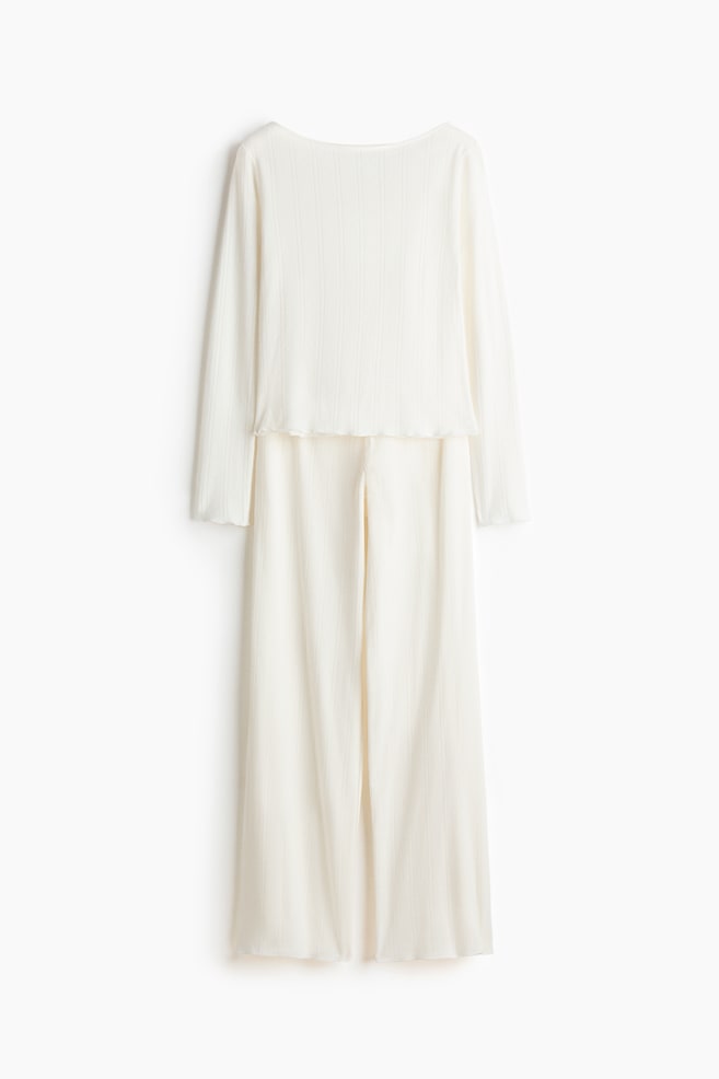 Un completo a due pezzi color crema presenta un top a maniche lunghe con un ampio scollo a barchetta, maniche lunghe con polsini ondulati sottili e un orlo ondulato, abbinato a pantaloni a gamba larga. Entrambi i capi mostrano una fine texture a coste verticali. - 1