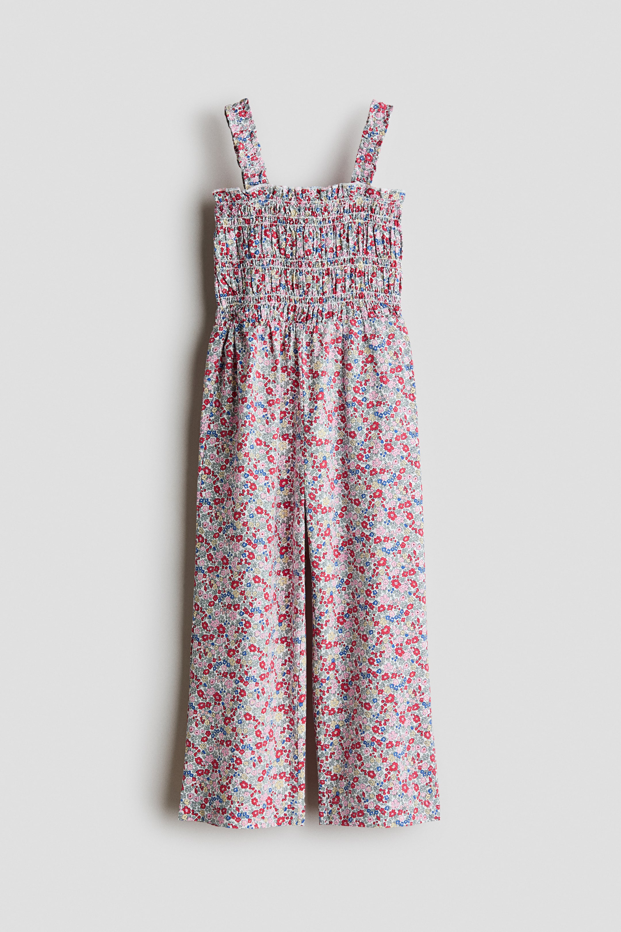 View larger image: This front-facing jumpsuit features an all-over floral print adorned with small red, blue, pink, green, and yellow flowers. It boasts a shirred bodice with wide shoulder straps, transitioning into wide-leg, cropped pants.