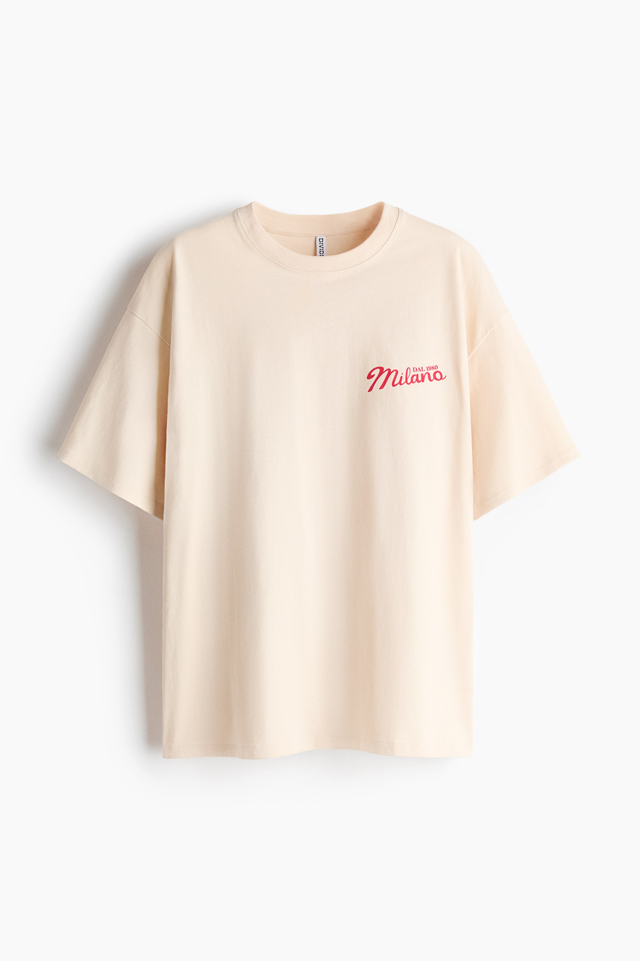 View larger image: A cream T-shirt is presented from the front, featuring a ribbed crew neck and short, loose-fitting sleeves. Red, stylised text reading 'DAL. 1980 Milano' appears on the upper-left chest.