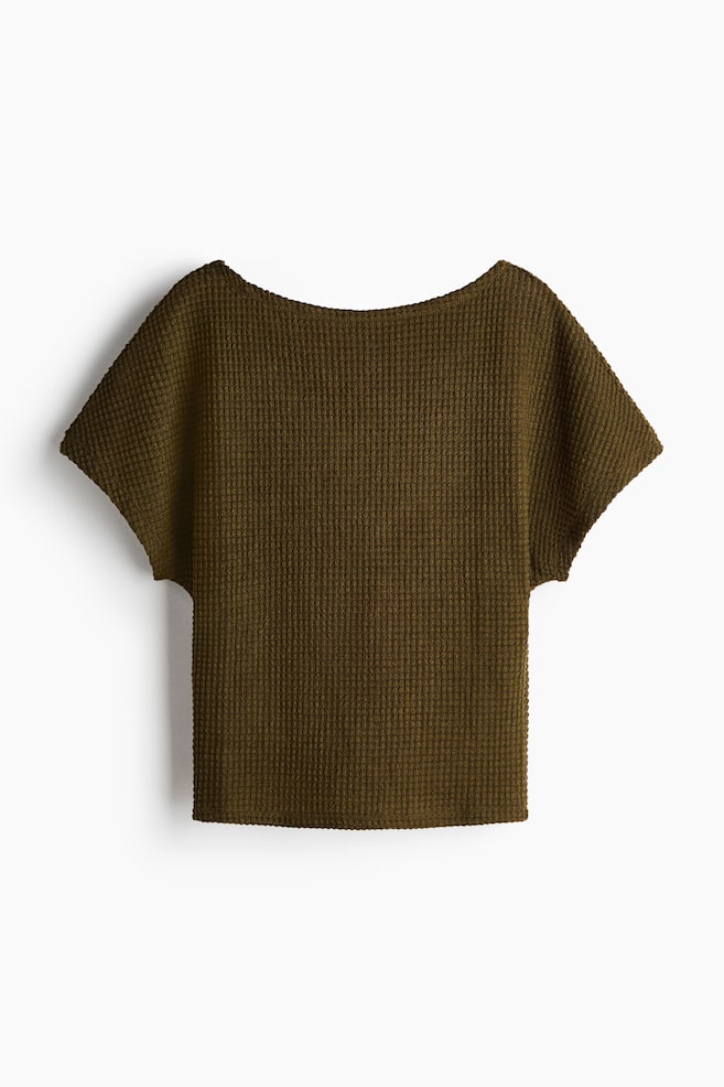The dark olive green top is featuring a prominent waffle knit texture. It is presenting a wide boat neckline, short dolman sleeves, and a straight hem. - 1