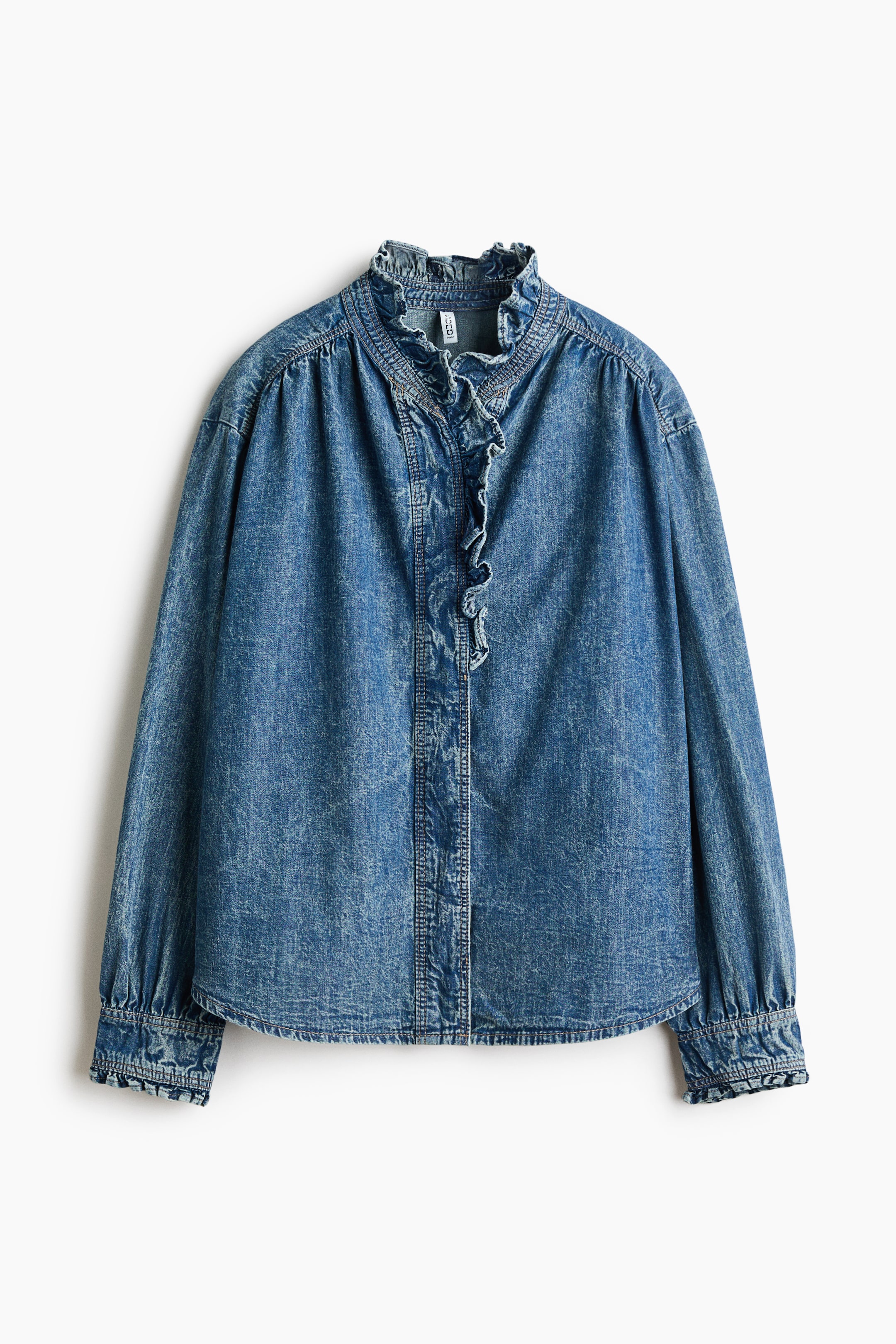 Grotere afbeelding bekijken: Een denim blouse in mediumblauw met een opstaande kraag met ruches en een voorpand met ruches. Het model heeft lange mouwen met geplooide schouders en manchetten met ruches, en een afgeronde zoom, alles met een faded wash.