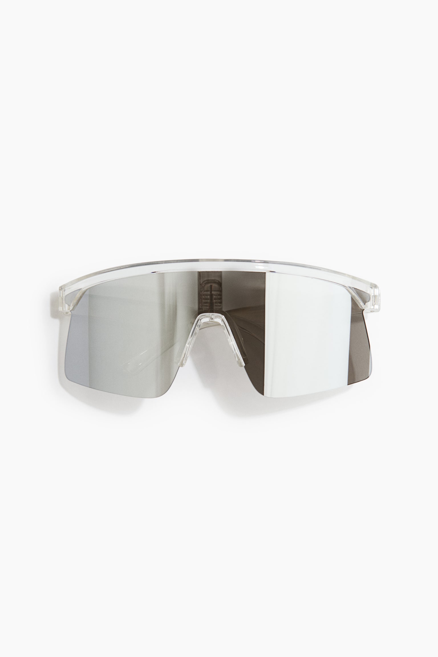 Actieve zonnebril met een transparant polycarbonaat montuur, weergegeven van voren. De zonnebril heeft een grote, uit één stuk bestaande zilverkleurige spiegelende lens met een sterk reflecterende afwerking en een geïntegreerde transparante neusbrug.