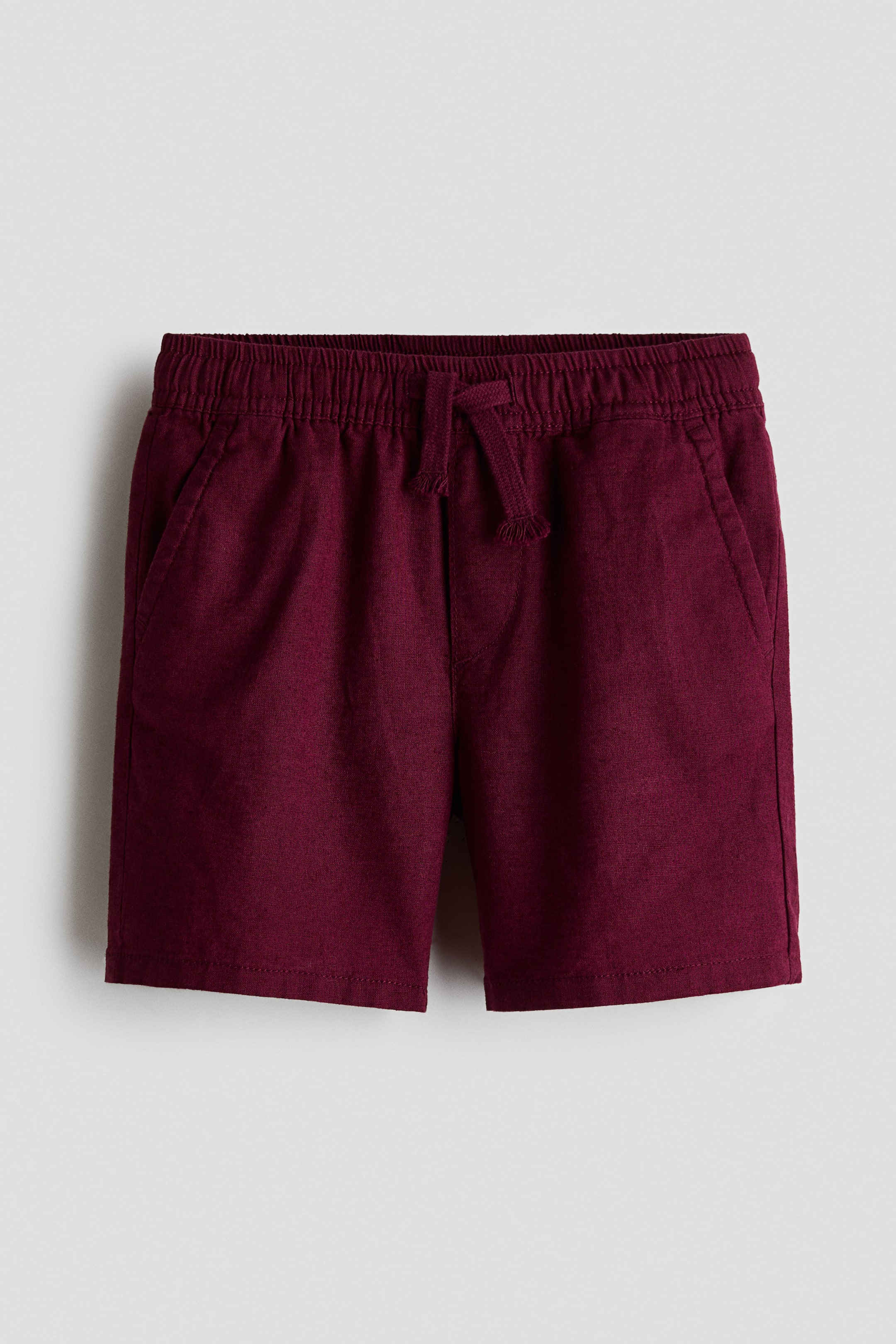 Xem ảnh lớn hơn: Quần short màu đỏ burgundy được làm từ chất liệu vải pha linen có bề mặt dệt nổi, được chụp từ phía trước, với cạp chun và dây rút cùng màu thắt ở giữa. Quần có túi xéo hai bên và đường may giả khóa kéo phía trước.