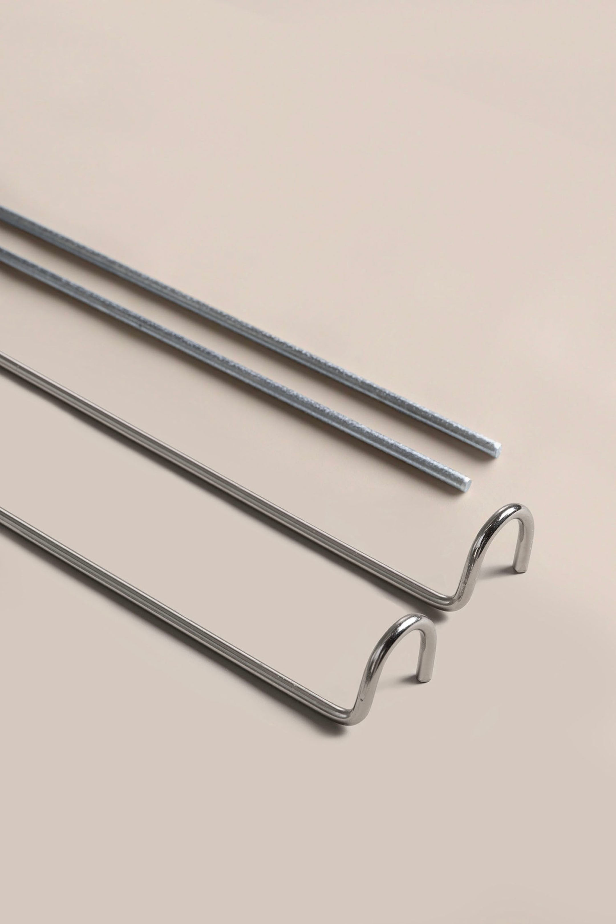 Größeres Bild ansehen: Vier Metallstangen liegen diagonal. Die beiden oberen Stangen erscheinen gerade und strukturiert, während die beiden unteren Stangen glatt und poliert wirken, wobei jedes Ende eine Hakenform bildet.